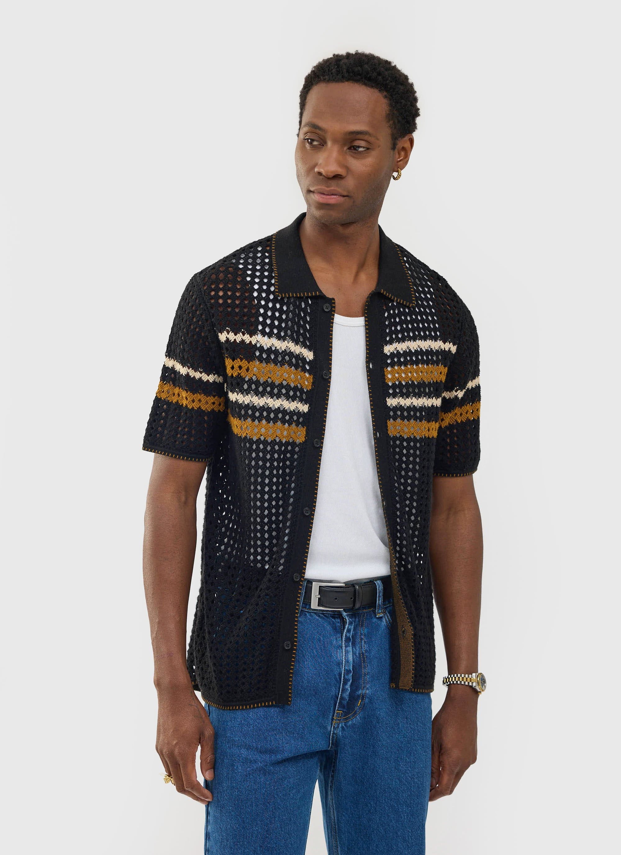 A man models the black Percival Pesaro Knitted Shirt, featuring a crochet design with yellow and cream chest stripes.
