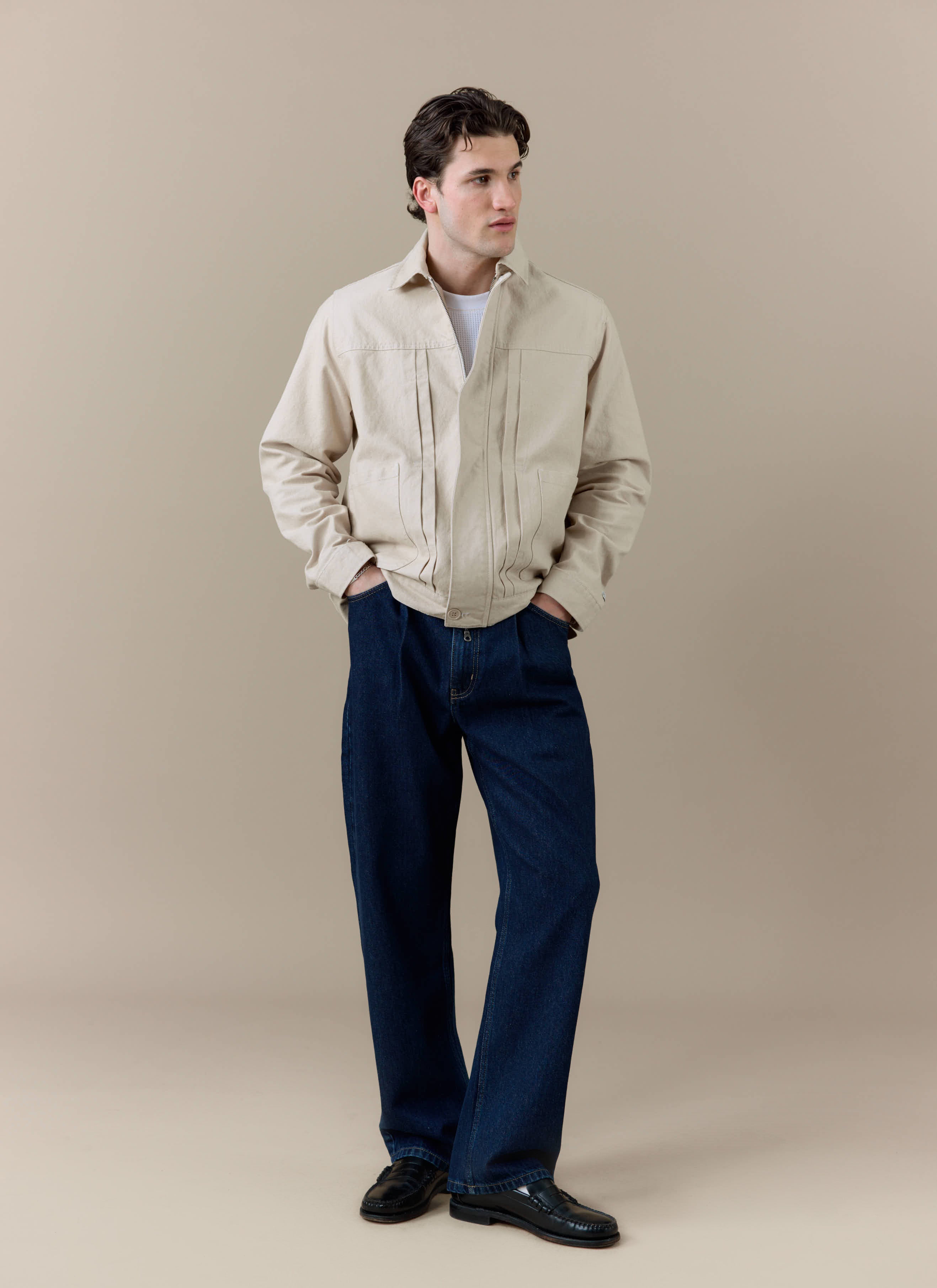 A model wearing the cream cotton Ernst Jacket by Percival, styled with dark blue denim trousers and black loafers.
