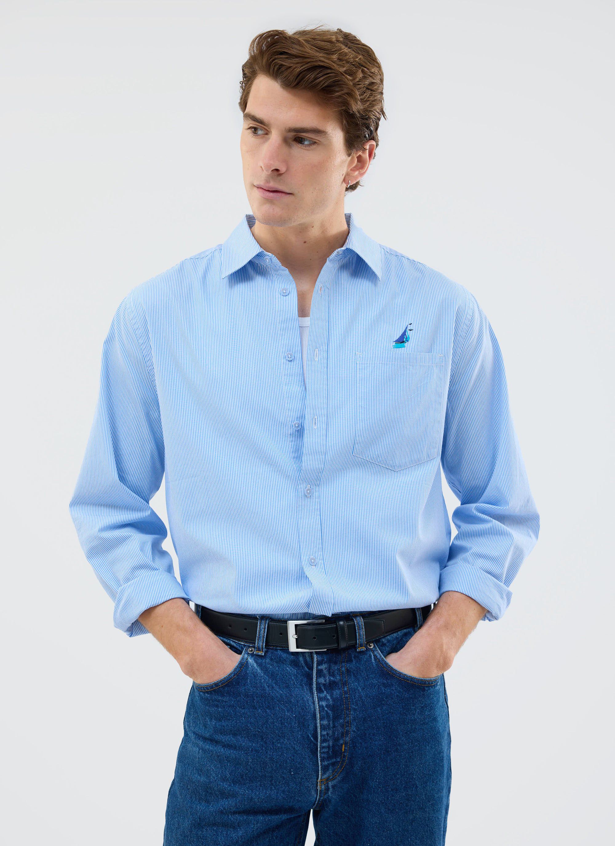 A model wears the Percival Yacht Stripe Oversized Shirt in blue, styled with dark denim jeans against a plain background.