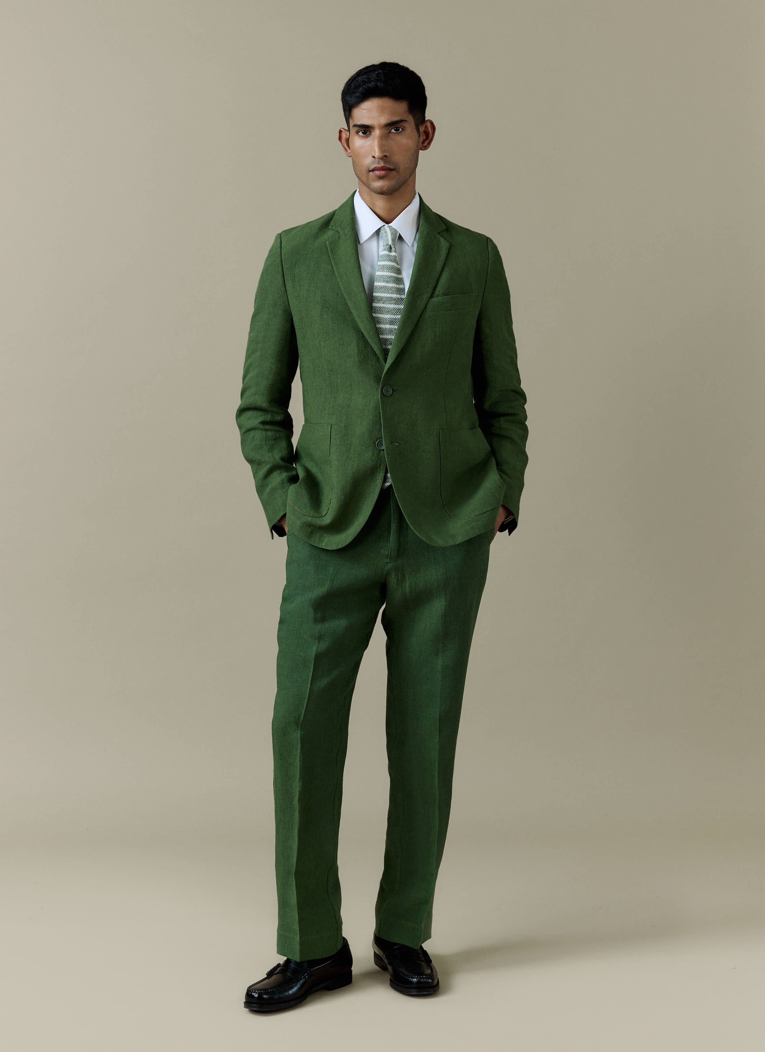 Forest green Percival tailored linen blazer and matching suit trousers, styled with a white shirt and patterned tie.