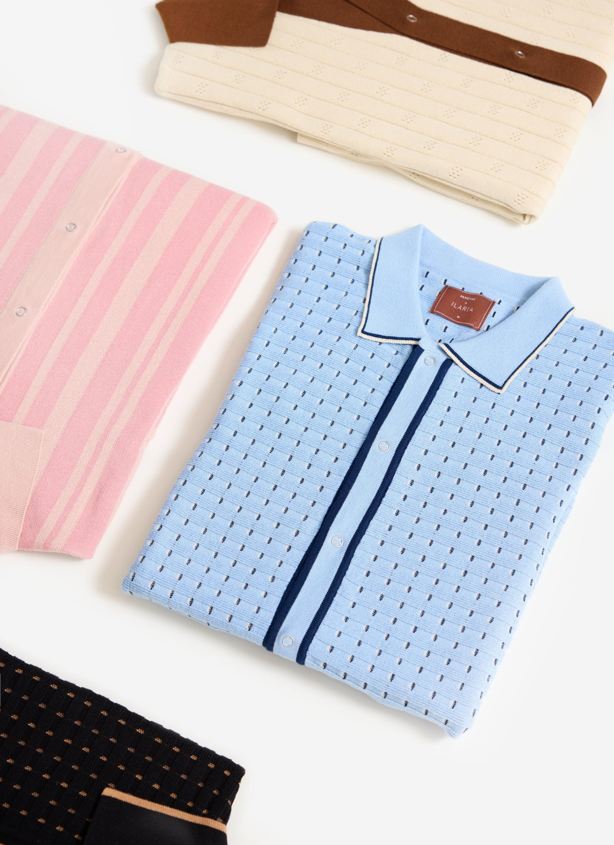 The Percival x Ilaria broken stripe knitted shirt in blue, folded with other shirts from the collection.