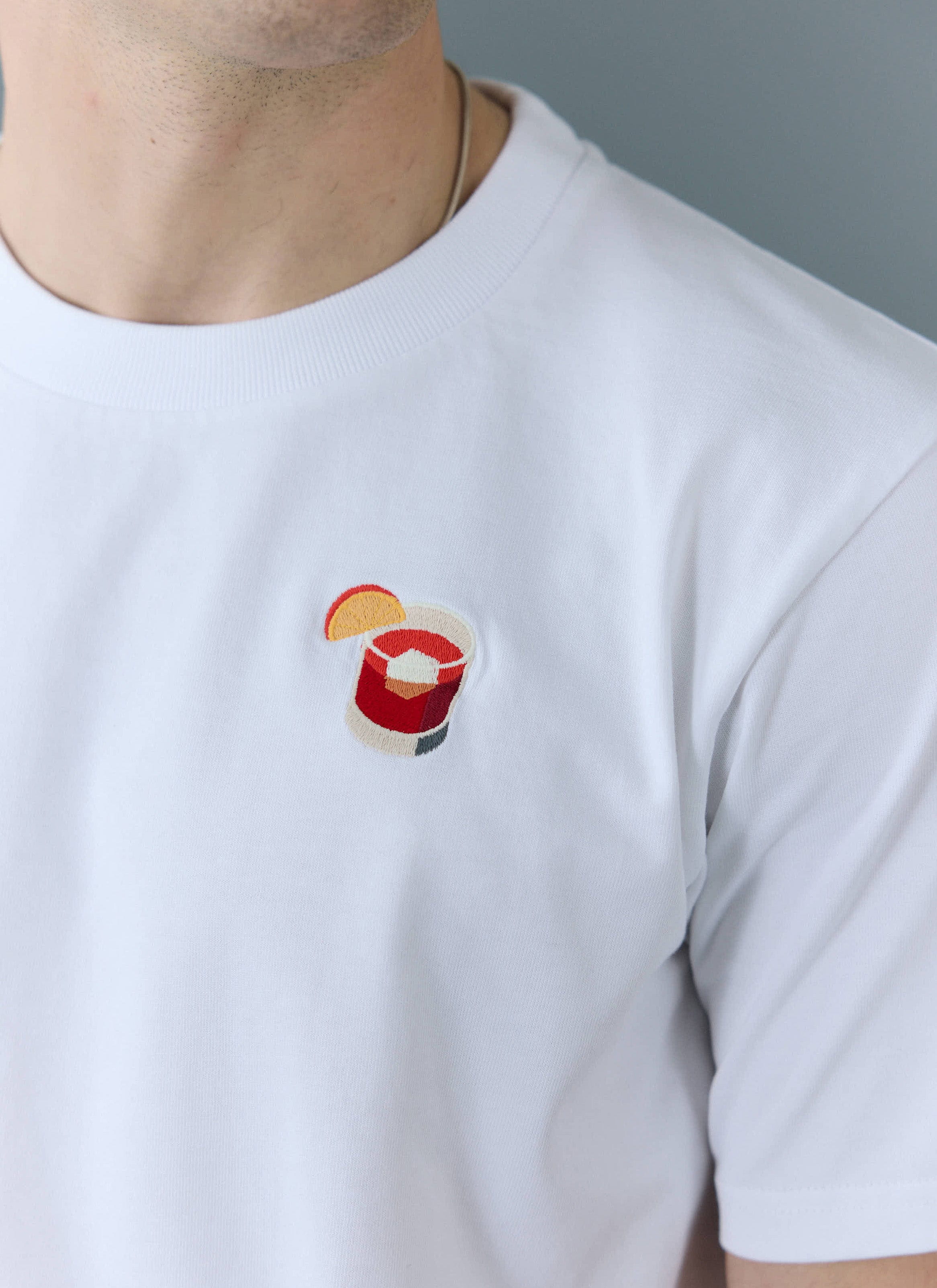 A close-up of the detailed Negroni cocktail embroidery on the chest of the white Percival T-shirt.