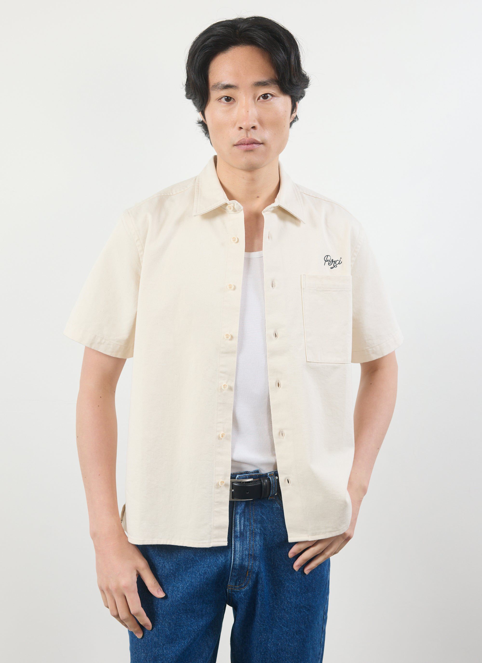 A model wears the Percival Olive Embroidered Cropped Shirt in off-white, styled open over a vest and blue jeans.