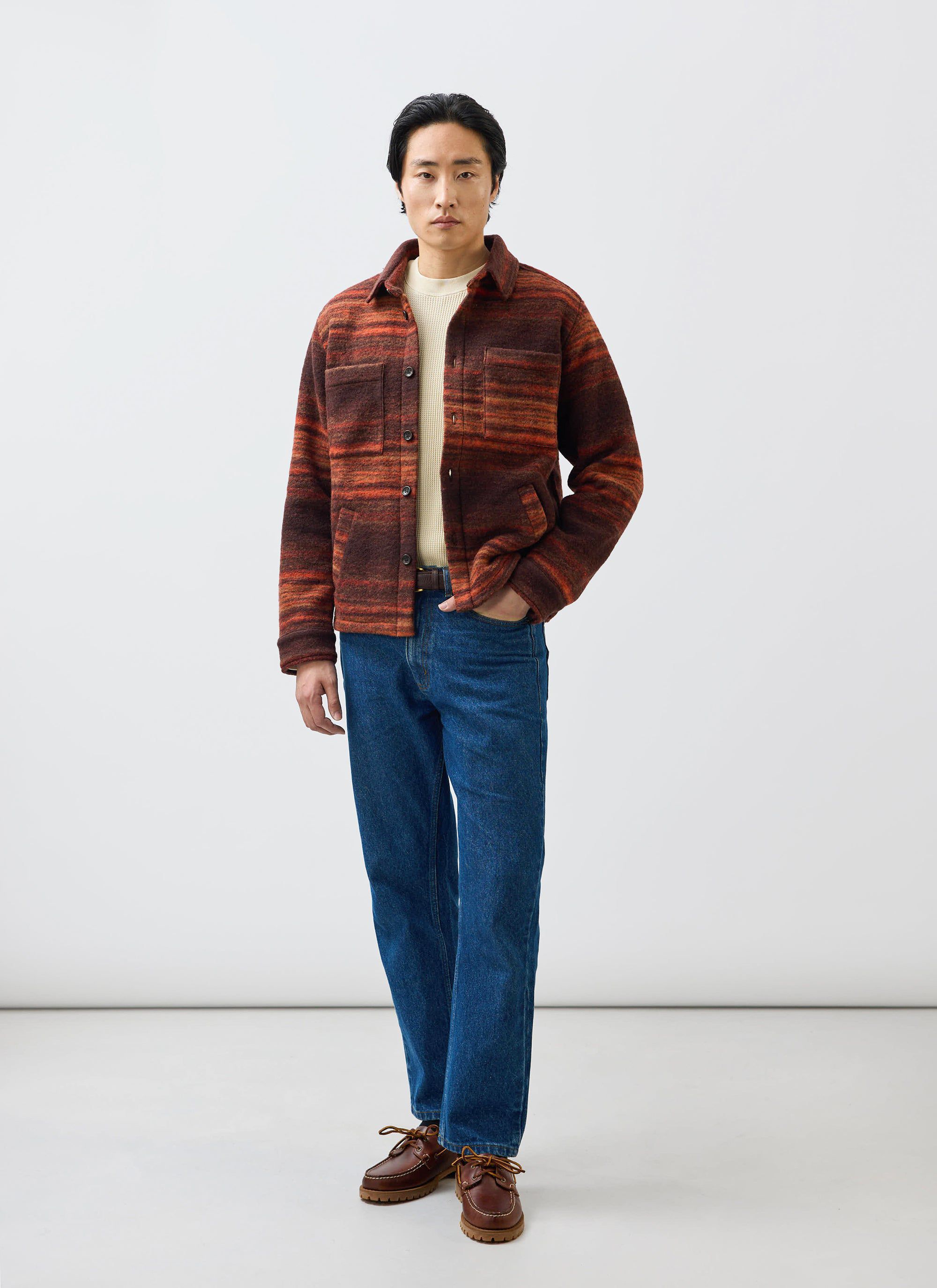 A model wears the Percival Mississippi Jacquard Overshirt in burnt orange and brown, styled with blue jeans and a cream knit.