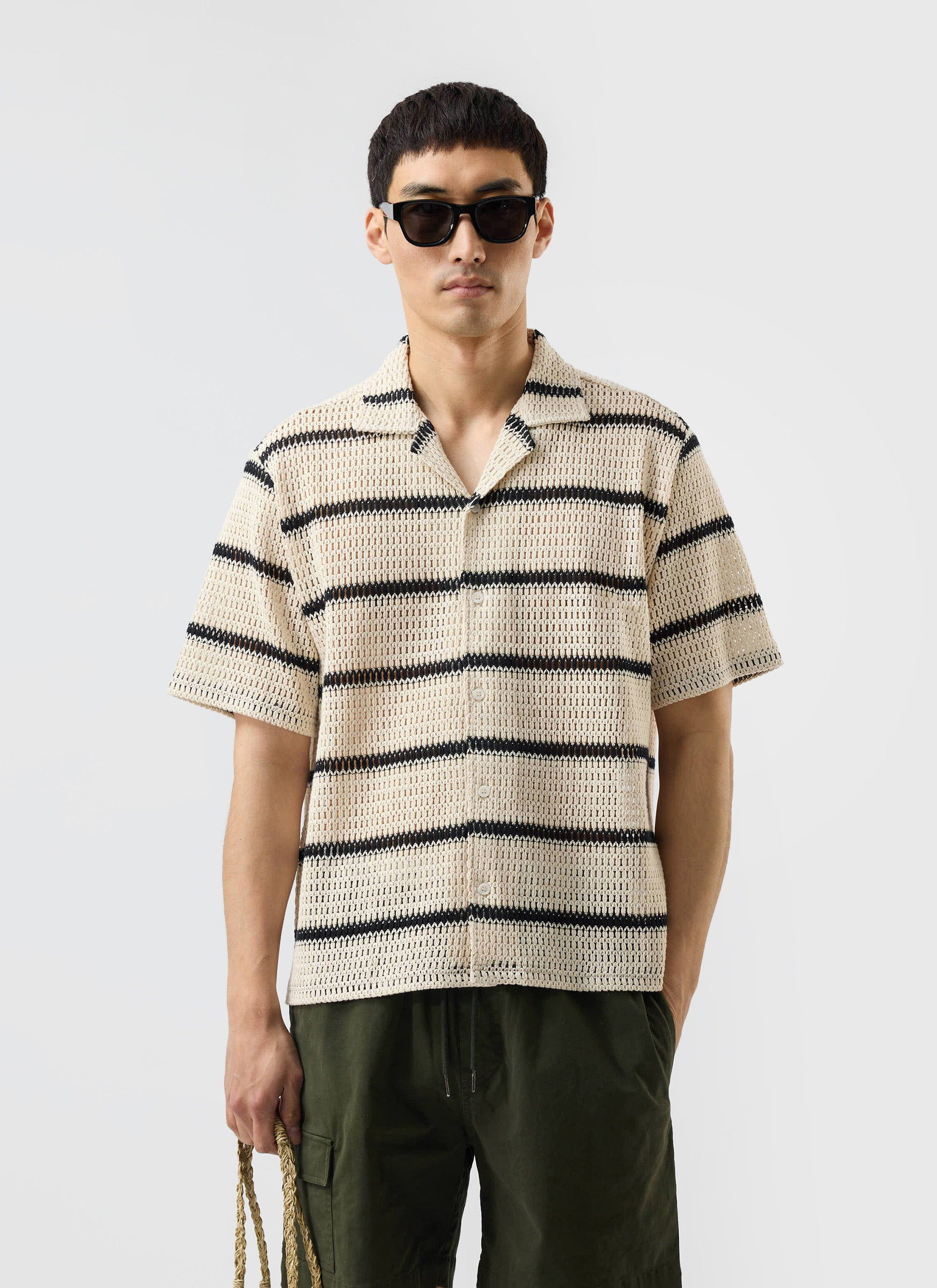 A model wears the Percival Crochet Groundsman Cuban Shirt in ecru with black stripes, styled with green cargo shorts.