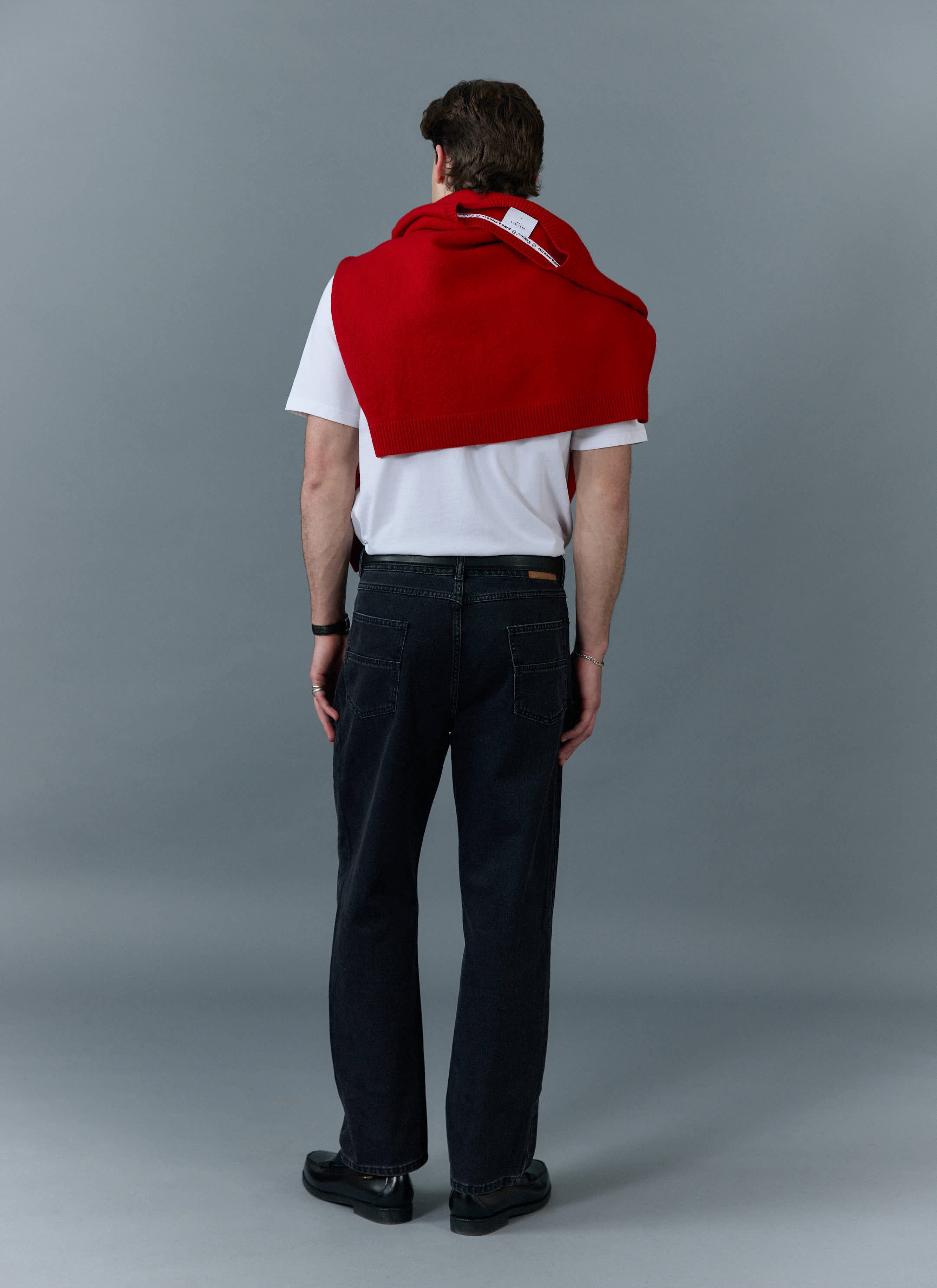 A model seen from behind wearing Percival black straight leg denim jeans with a white t-shirt and a red jumper.