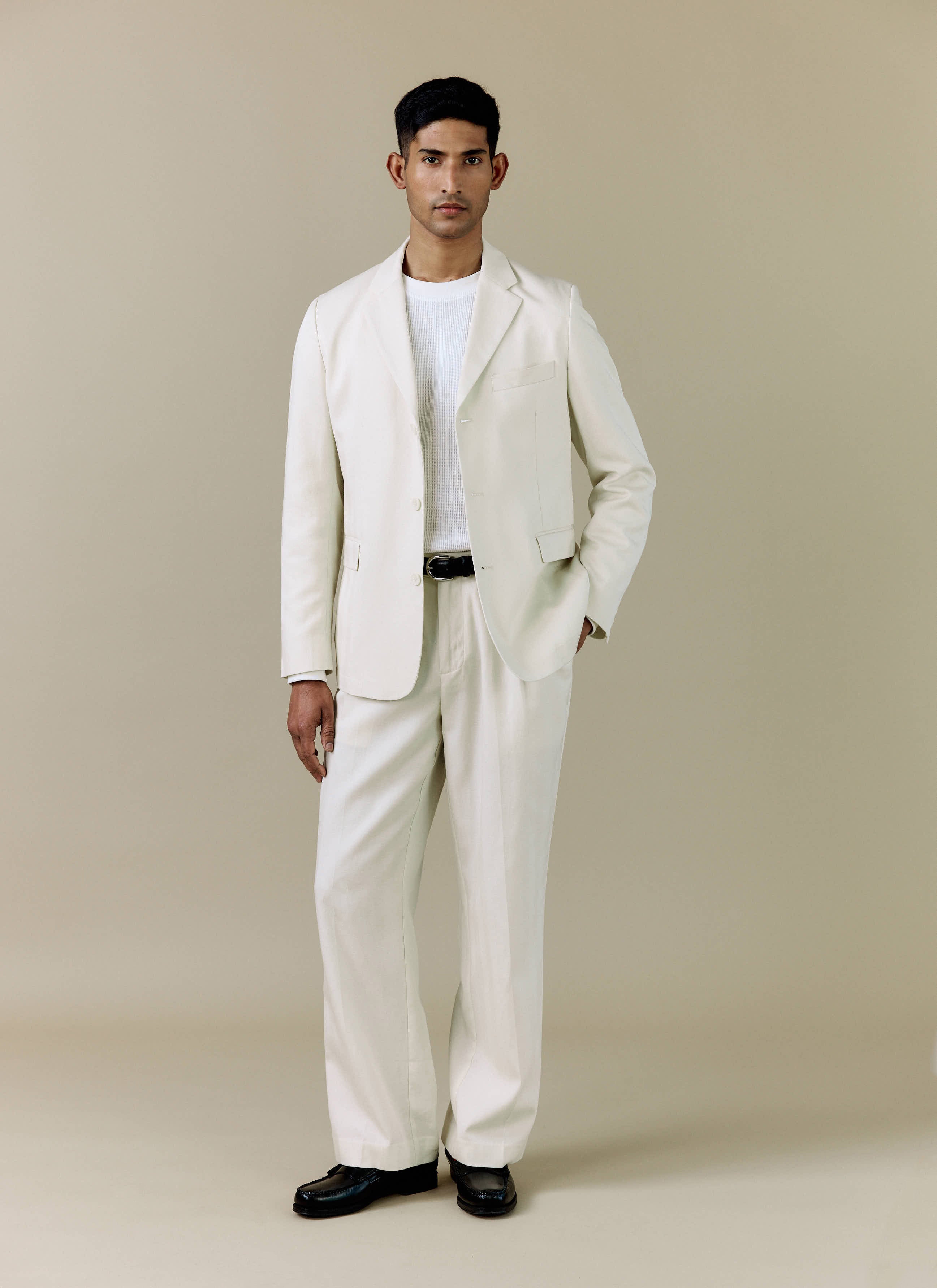 A model wears the Percival Pleated Tailored Trousers in cream, styled as a full suit with the matching blazer.
