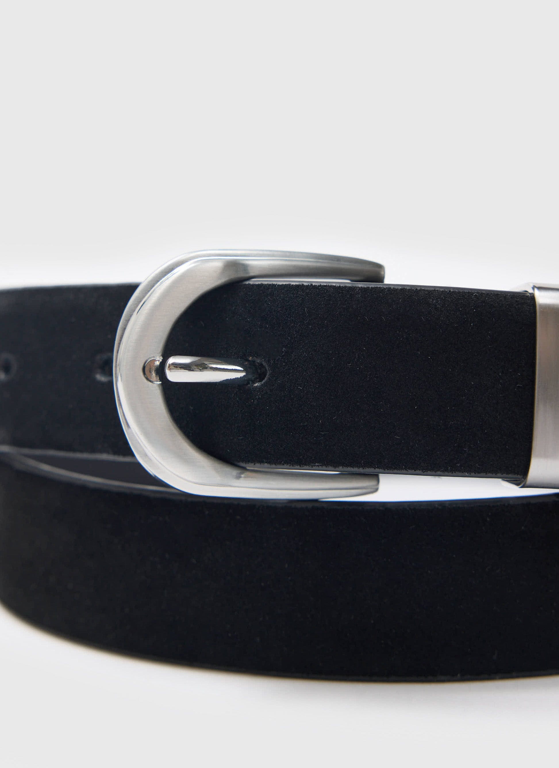 A detailed studio shot of the Percival black suede belt, focusing on the polished silver western-style buckle.