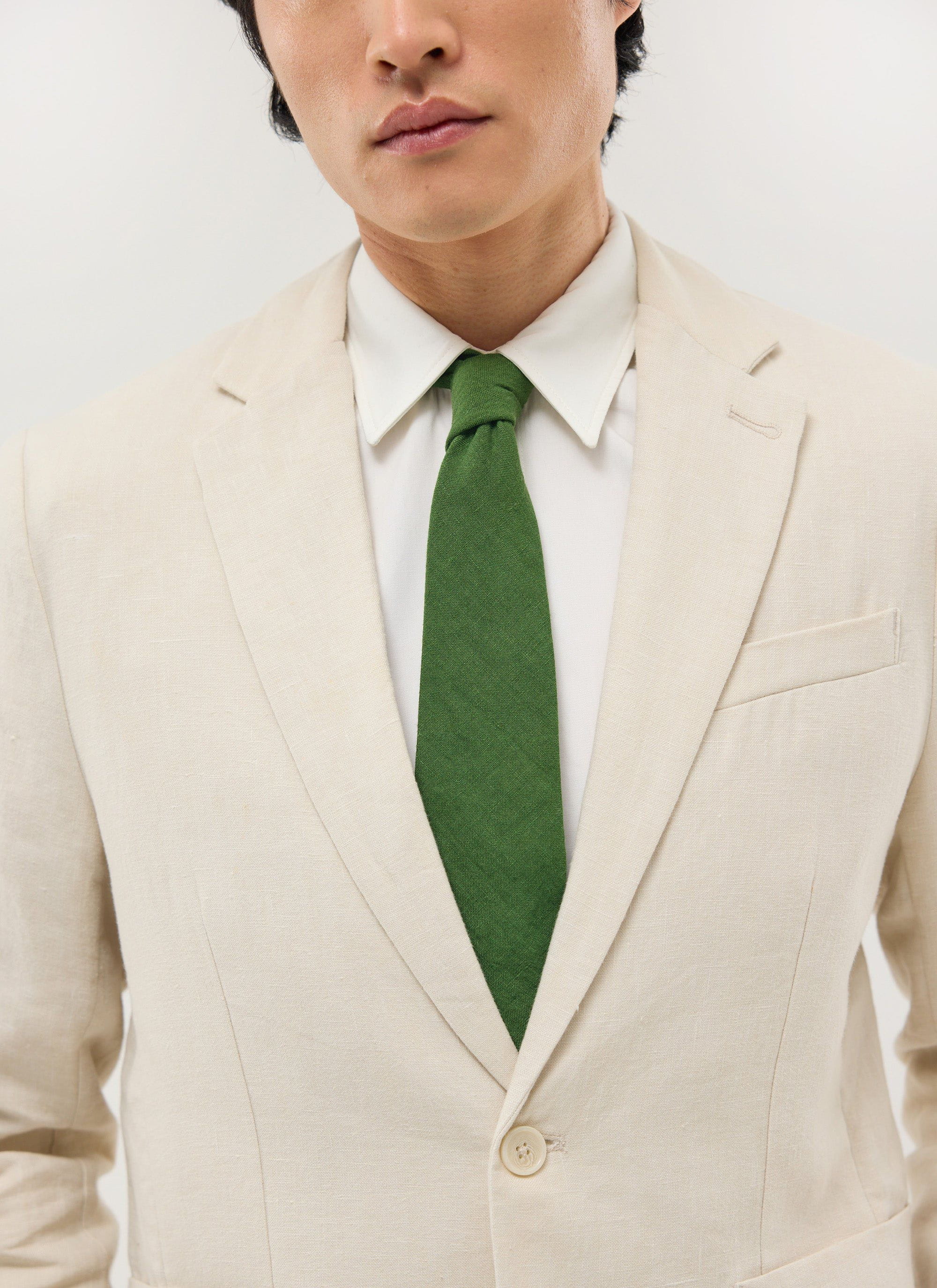 A man models the Percival Linen Tie in Forest Green, paired with a white shirt and a cream linen suit.