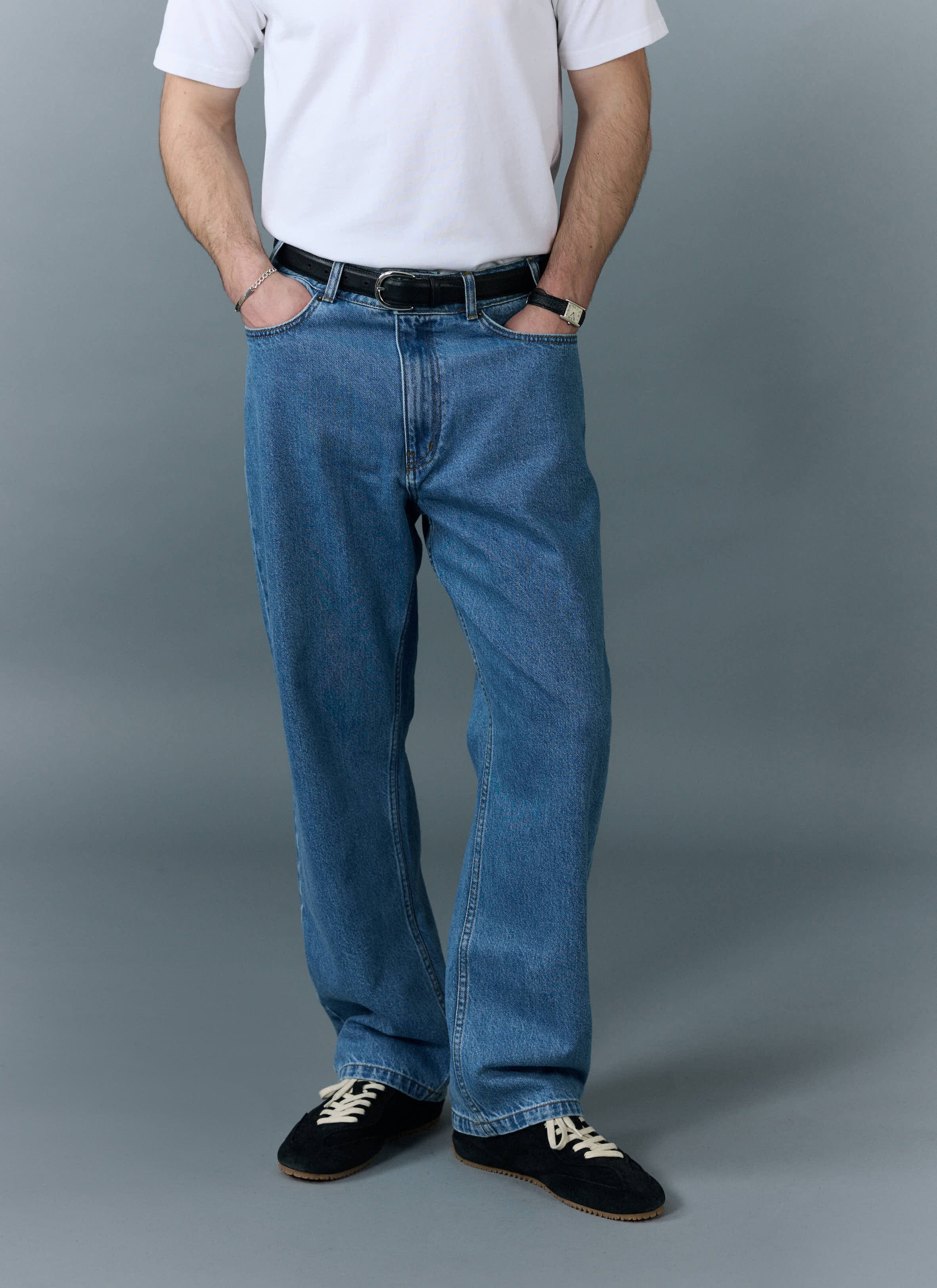 A model wears the Percival Wide Leg Denim Jeans in light wash blue with a white t-shirt against a grey background.