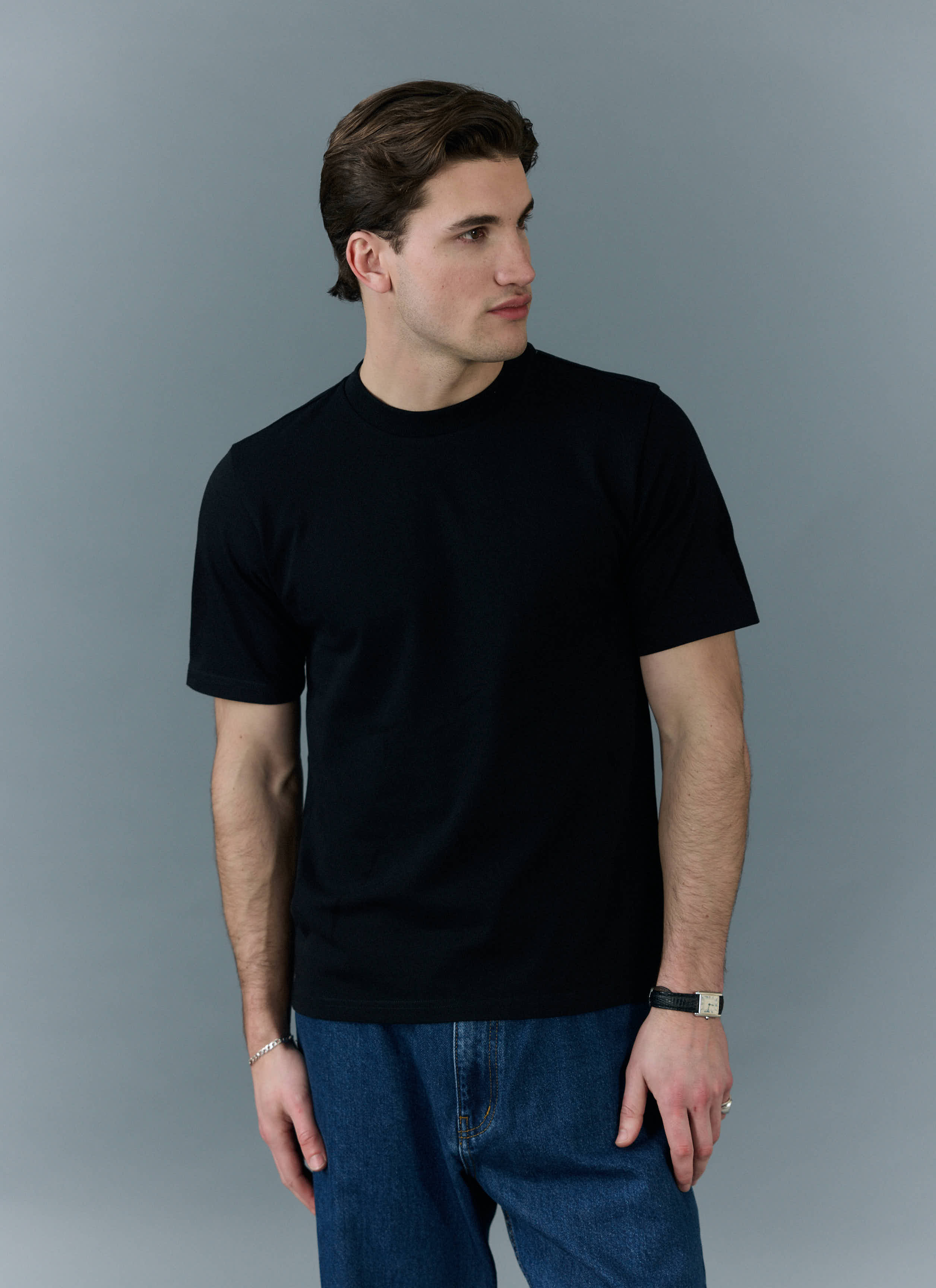 A man models the Percival black Cropped Regular Fit T-Shirt, styled with blue jeans against a simple grey background.