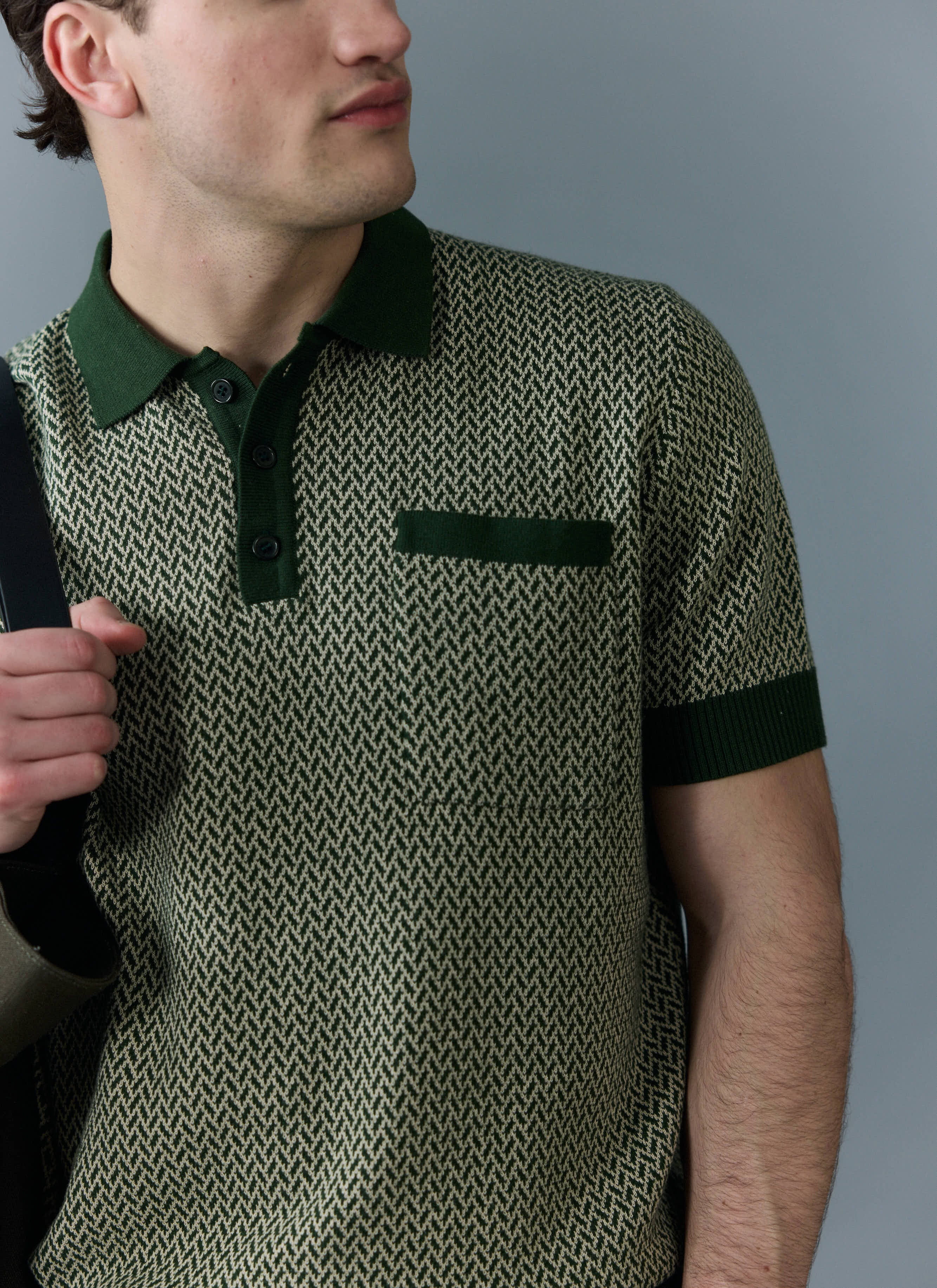 A man models the Percival Casa Martini Knitted Polo in forest green, which has a cream geometric pattern and a chest pocket.