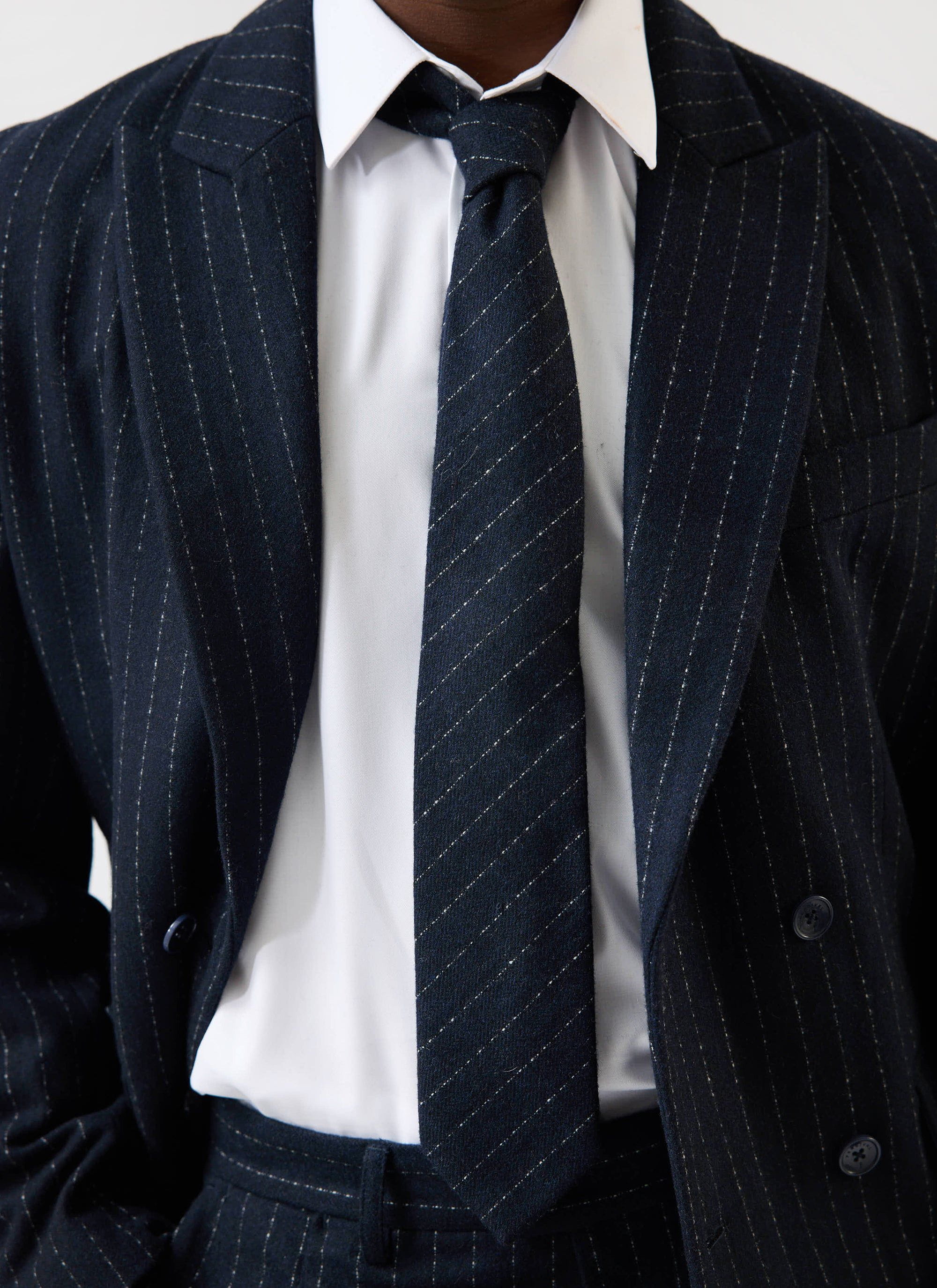 A model wears the Percival Textured Stripe Tie in navy, styled with a crisp white shirt and a matching navy pinstripe suit.
