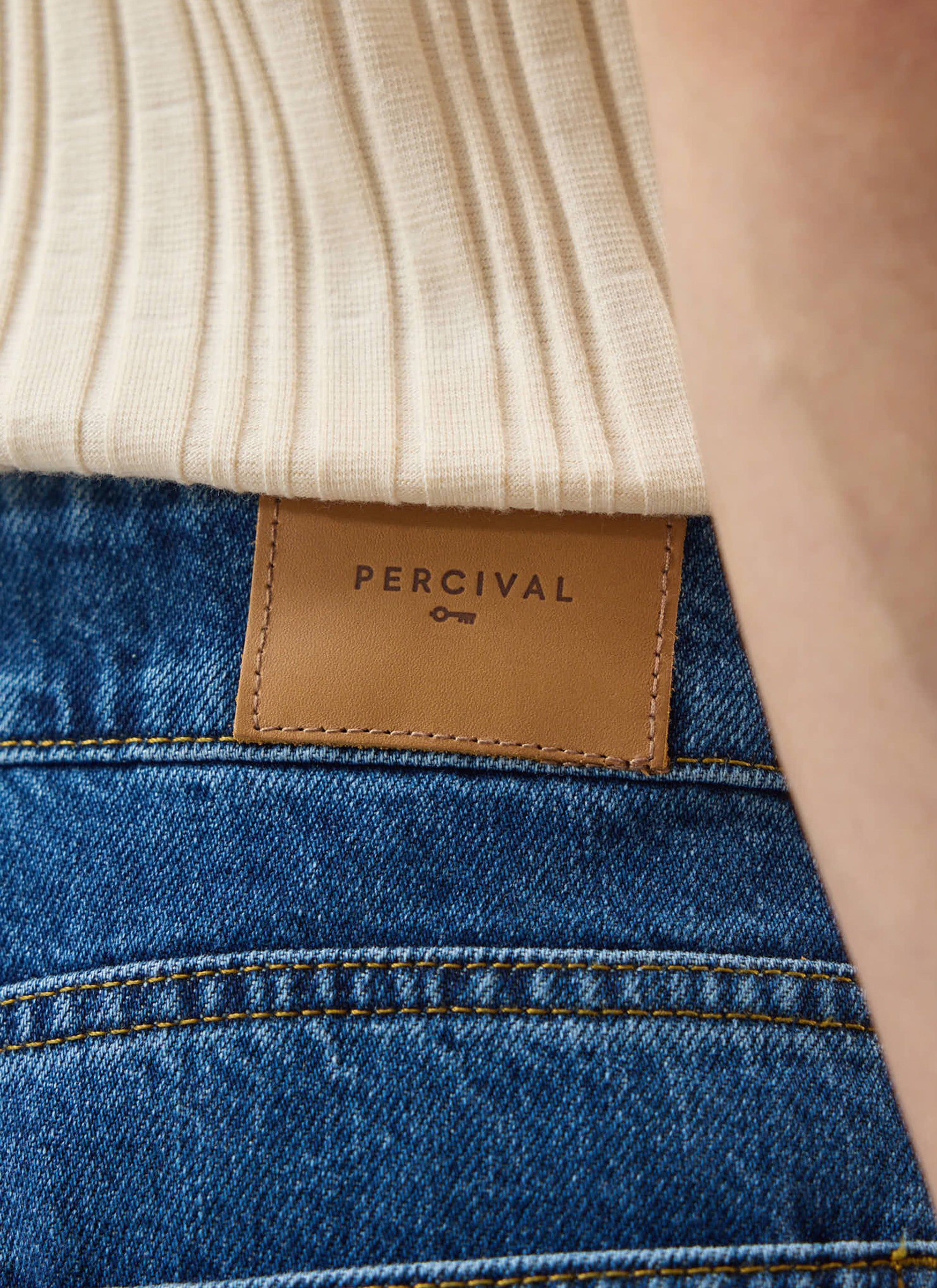 A detailed close-up of the branded tan leather patch on the back of the Percival Stay Press Denim Jeans in mid-wash blue.