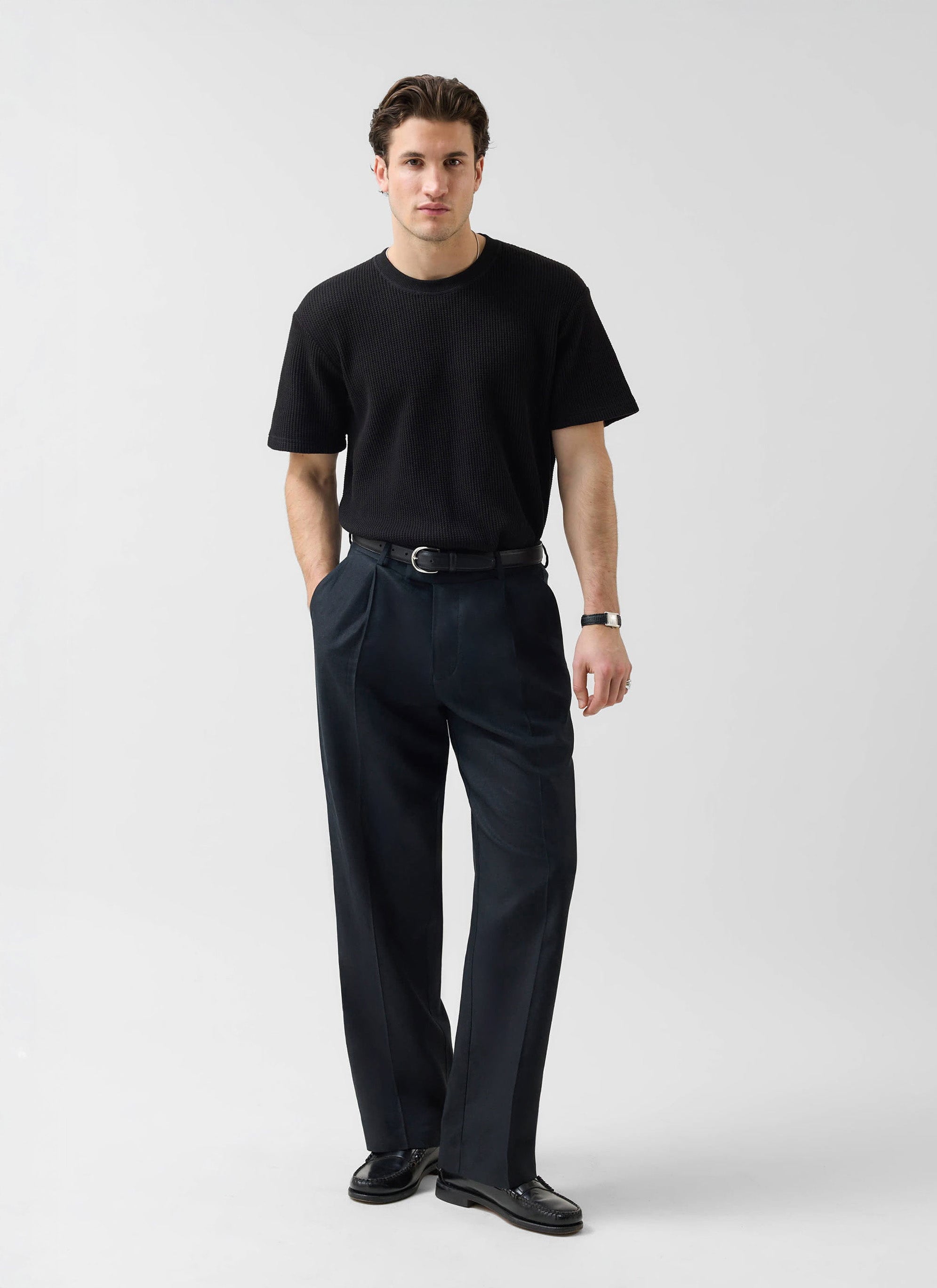 A model wears the Percival Wide Leg Trousers in black linen, styled with a black textured t-shirt and black loafers.