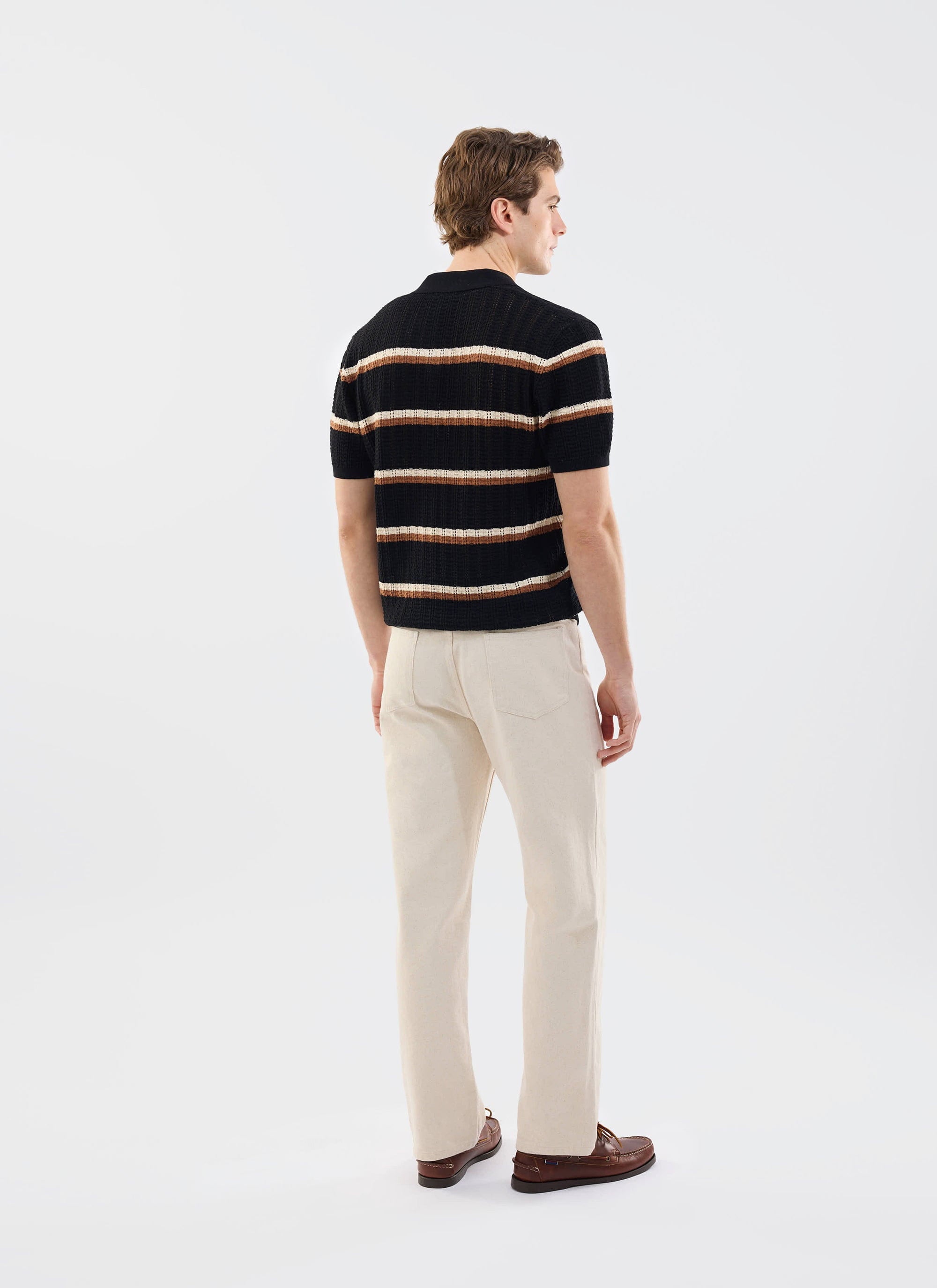 A man models the Percival Tessaro Knitted Stripe Polo in black with cream and brown stripes, seen from behind.