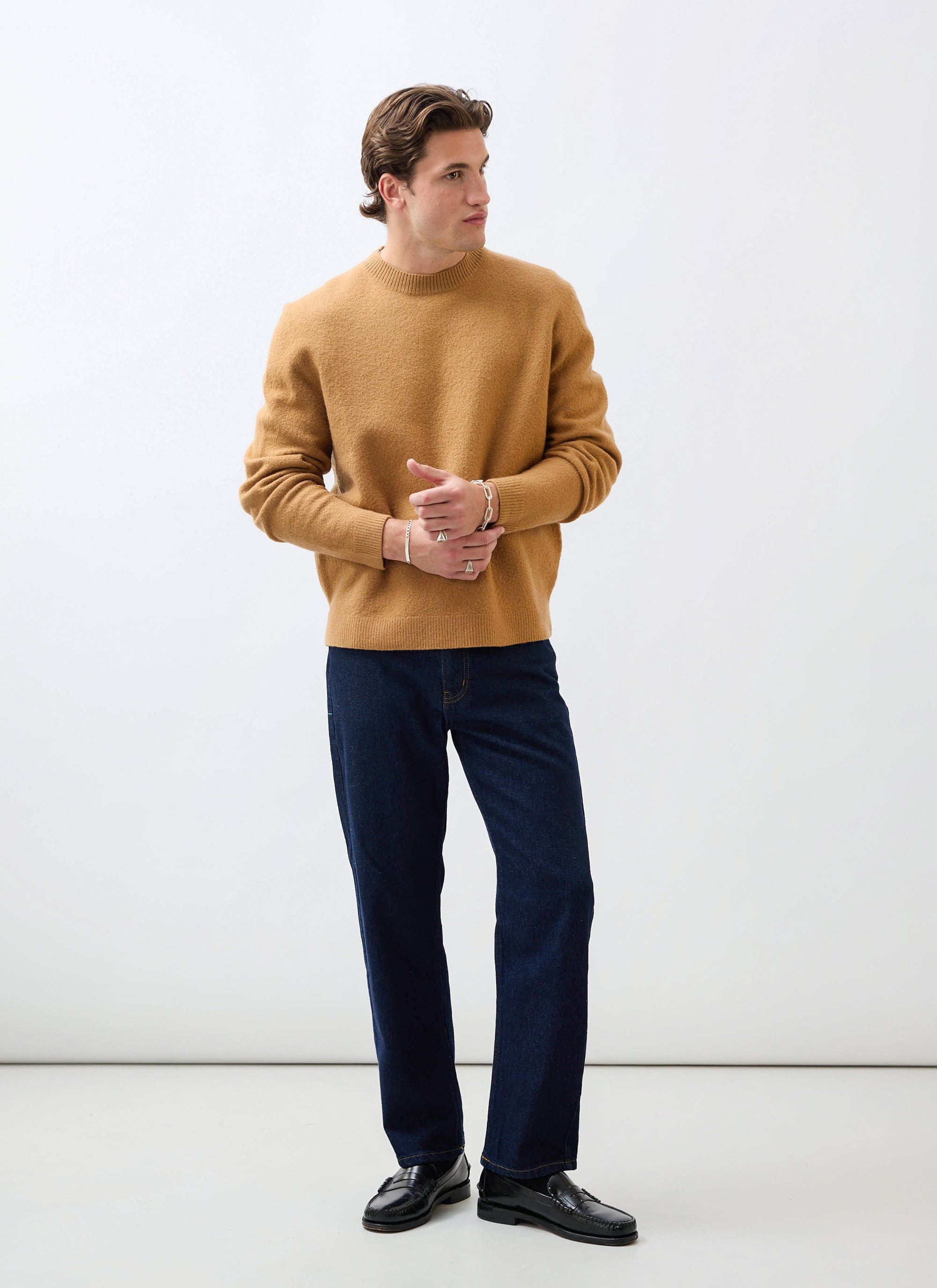 A model wears the brown Felted Wool Jumper from Percival with dark blue jeans and black loafers in a studio.