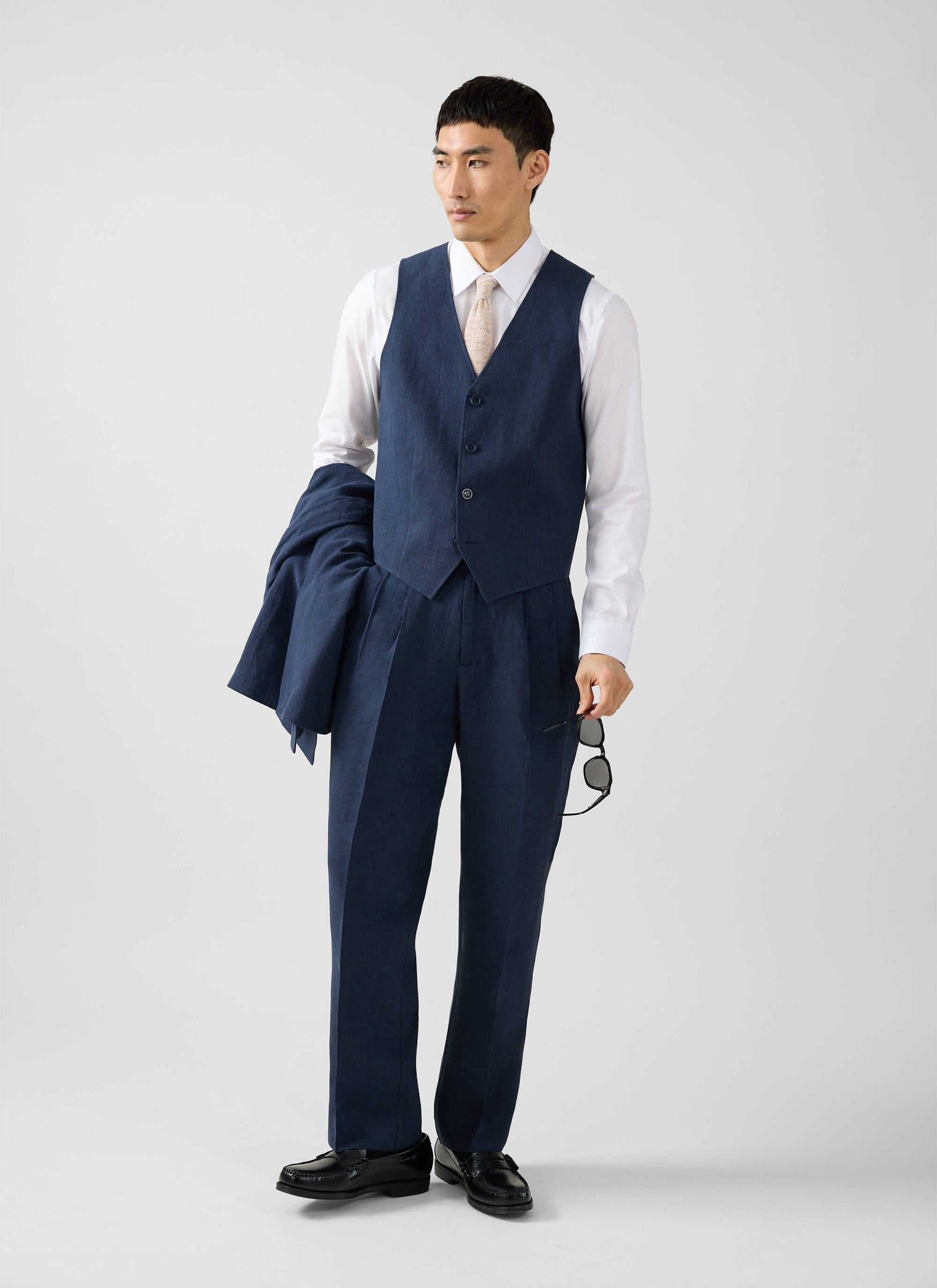 A man models the Percival navy linen waistcoat as part of a three-piece suit against a white studio background.
