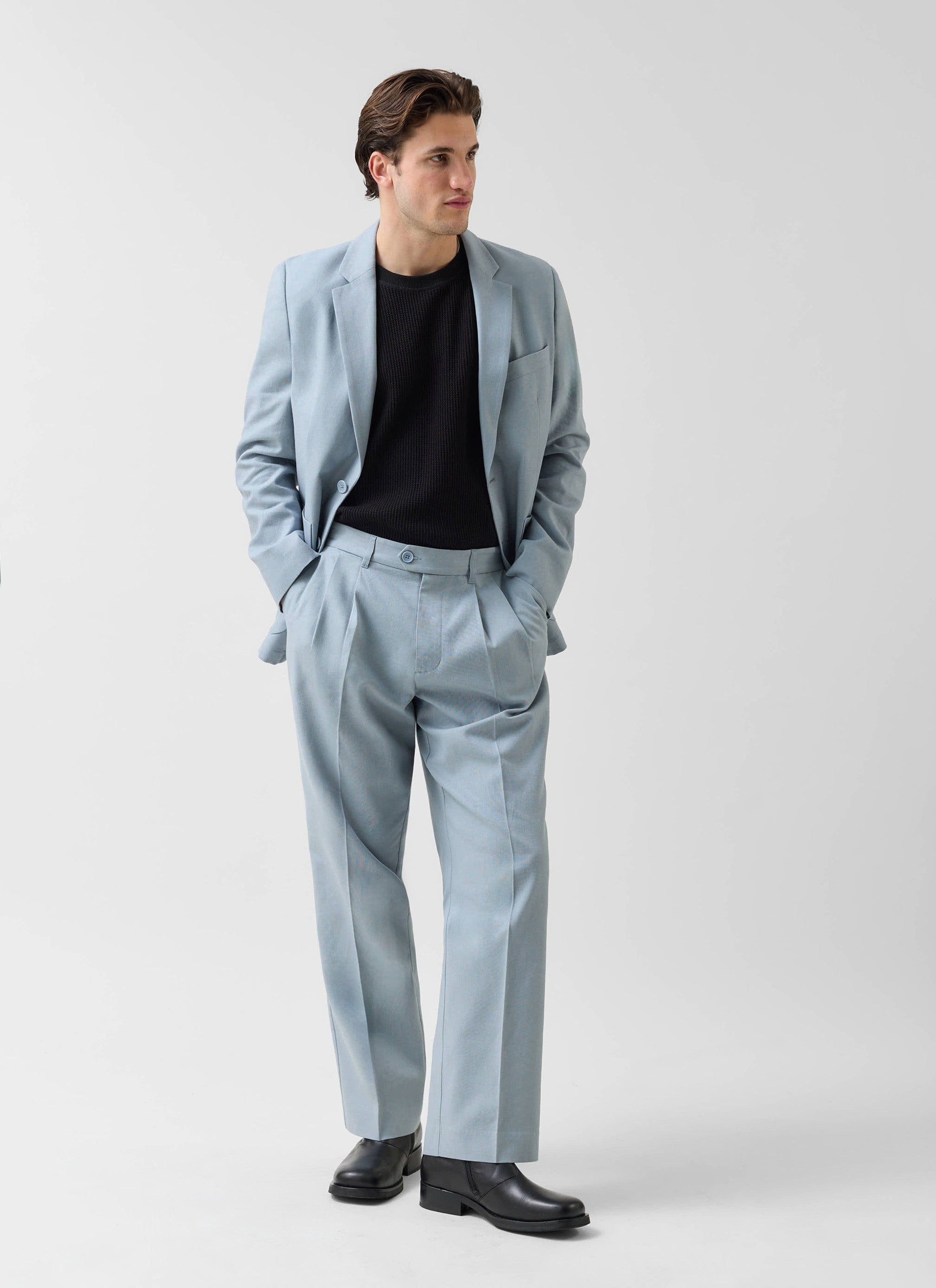 A model wears the Percival tailored linen suit in light blue, paired with a black knitted top and black leather boots.
