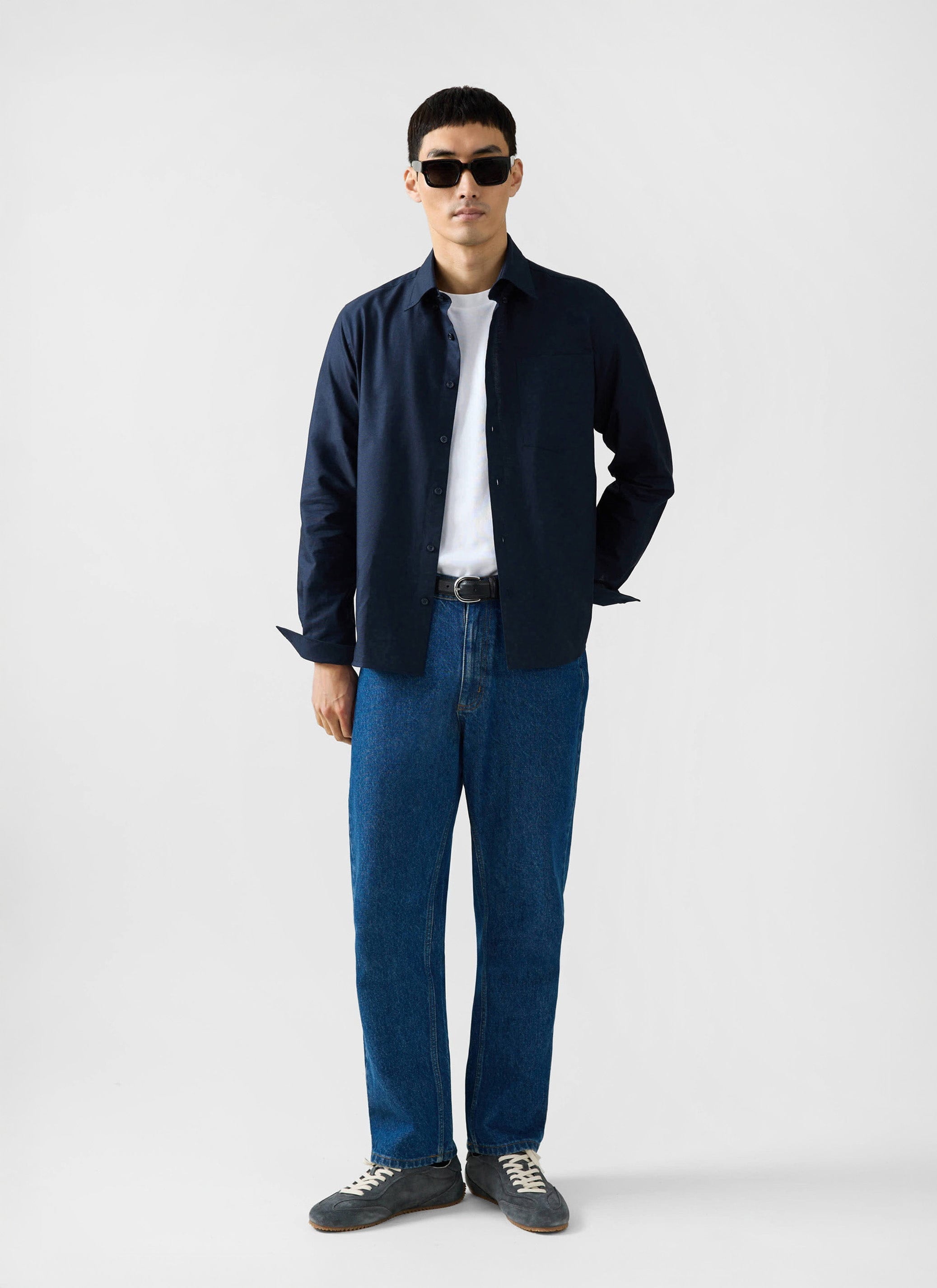 A model wears the Percival Oxford Regular Shirt in navy, styled open over a white t-shirt and blue jeans.