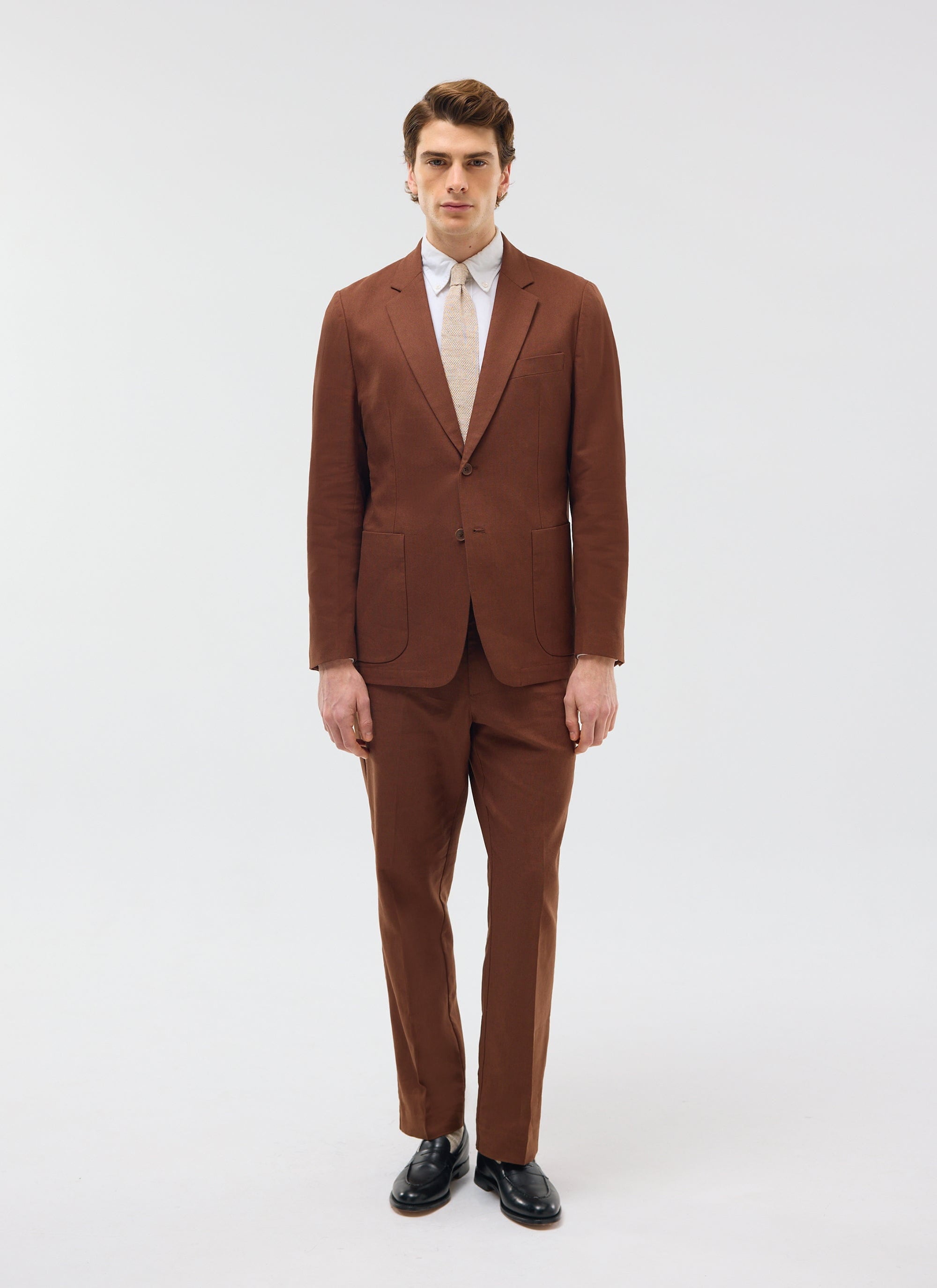 A model wears the Percival Tailored Linen Trousers in brown, styled with the matching blazer against a white background.