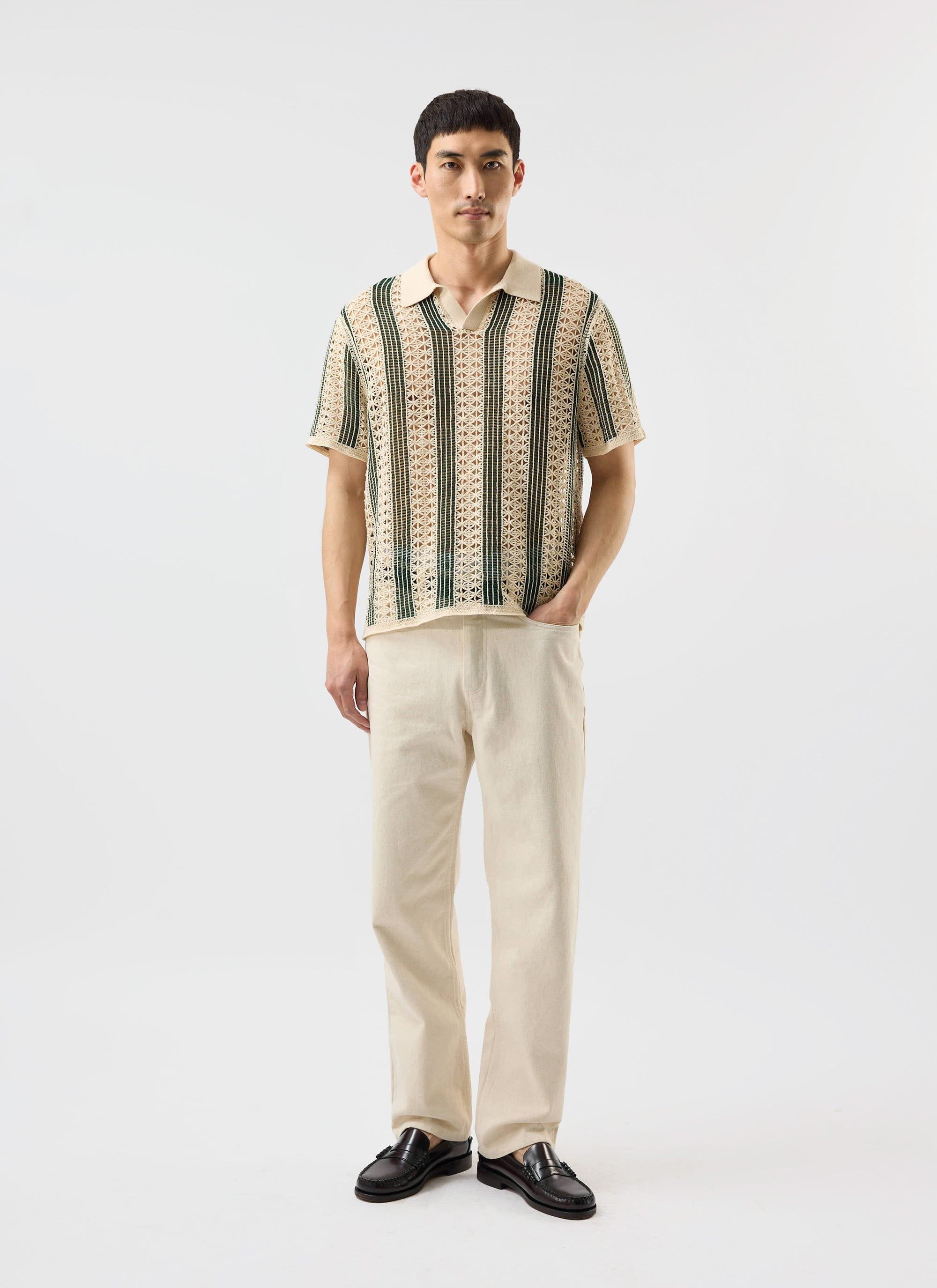 A man models the Percival Sarti Knitted Polo Shirt in ecru with forest green stripes, paired with cream trousers.