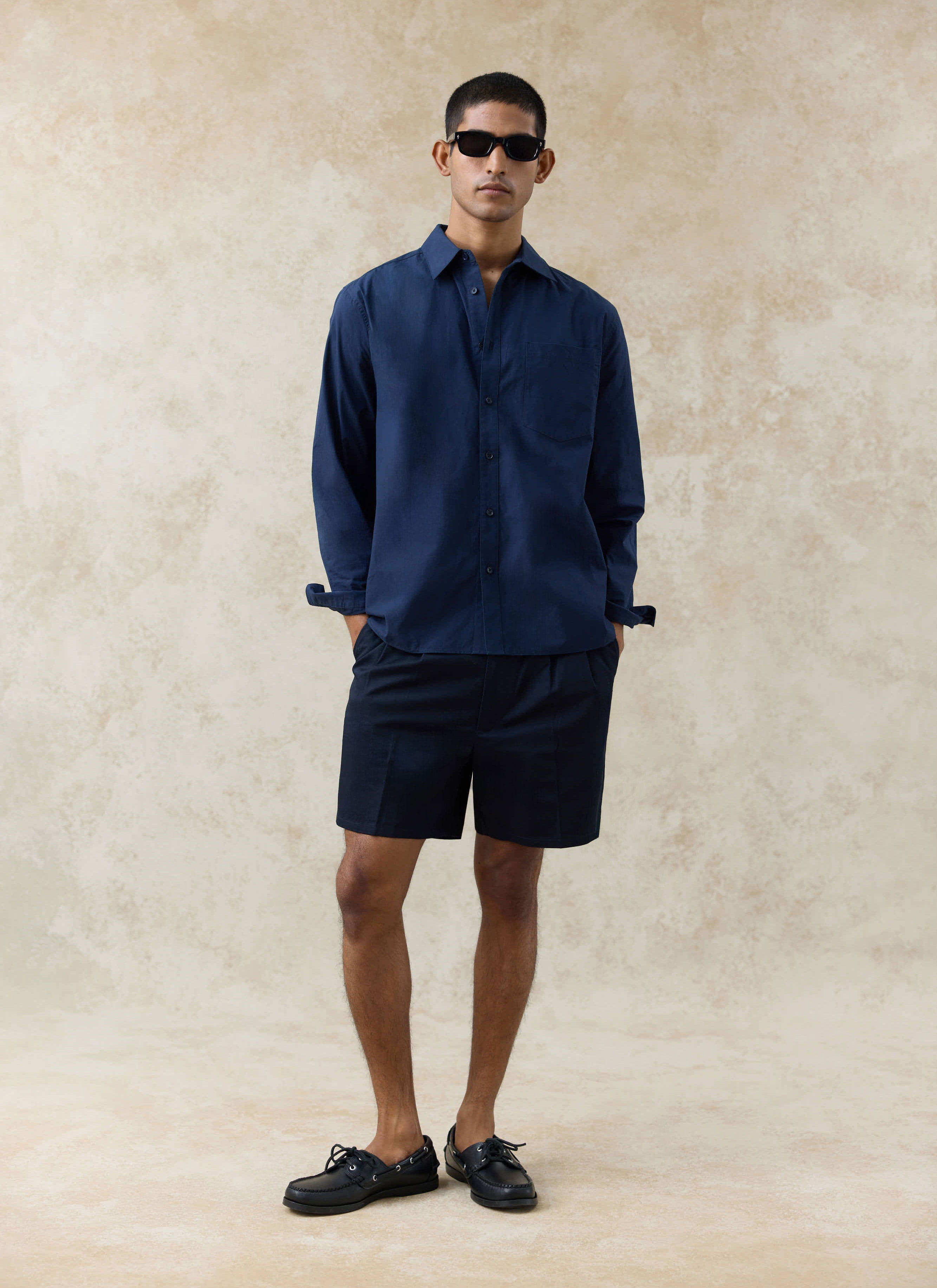 Navy Percival Dali Poplin Shirt and matching Blake Double Pleated Shorts worn by a model against a textured backdrop.