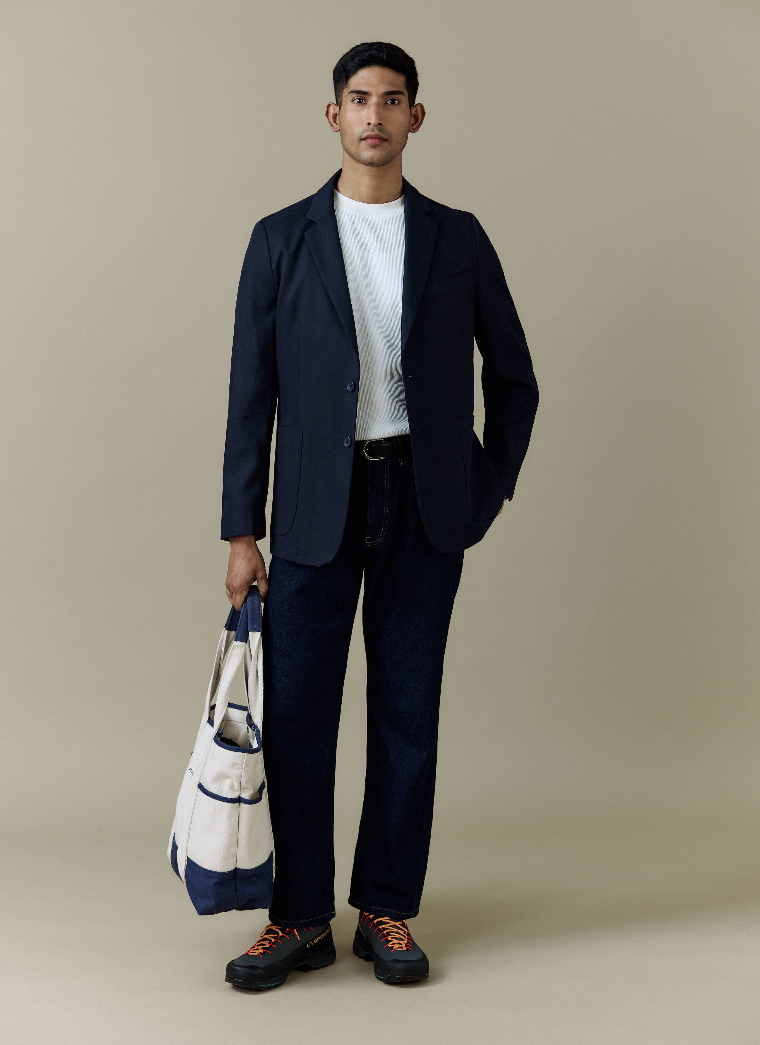 A model wears the navy Lyocell Regular Blazer by Percival, styled with a white tee, dark jeans, and holding a tote bag.