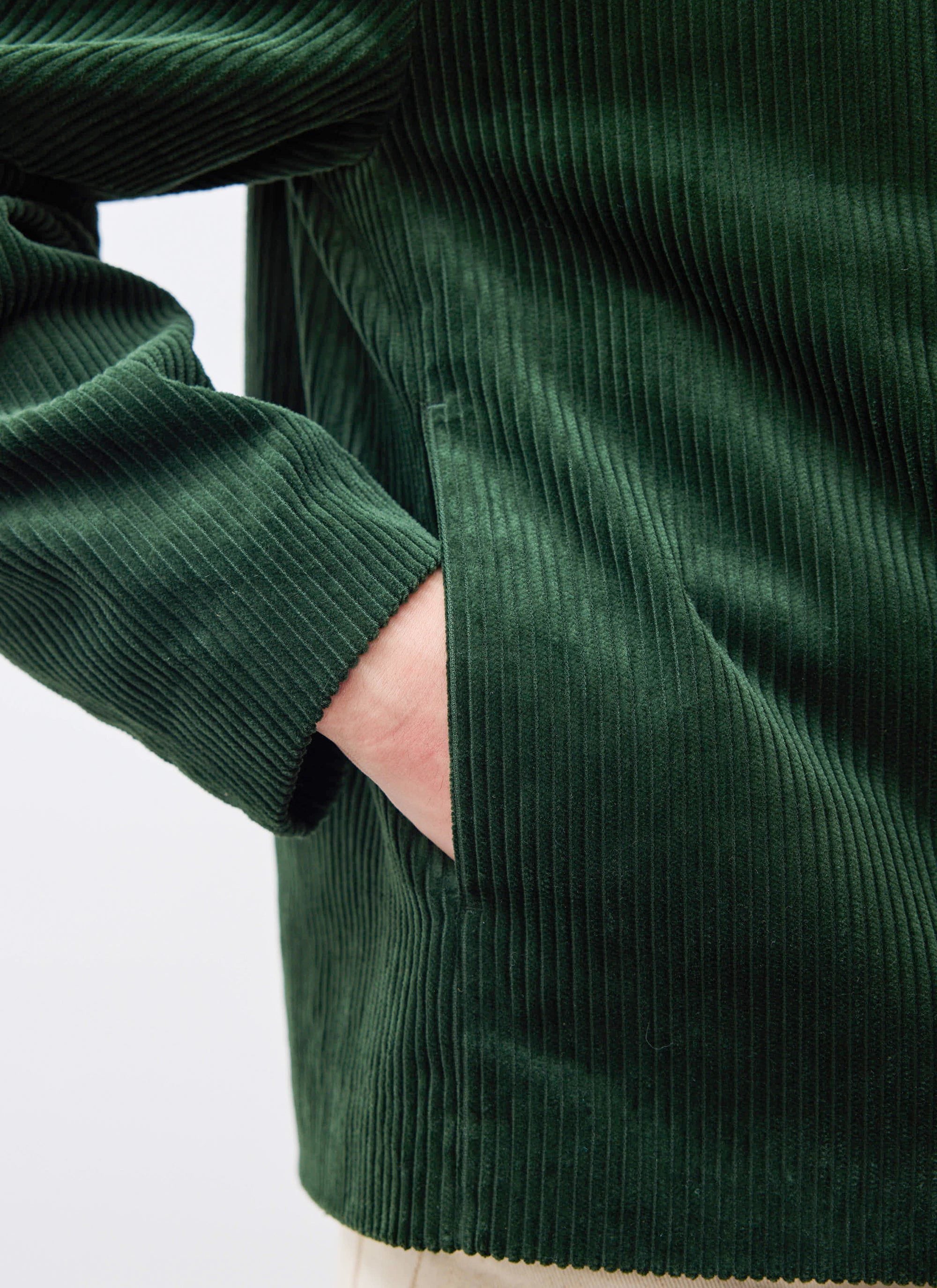 A close-up of a model's hand in the pocket of the Percival Cord Overshirt in forest green, showing the cord texture.