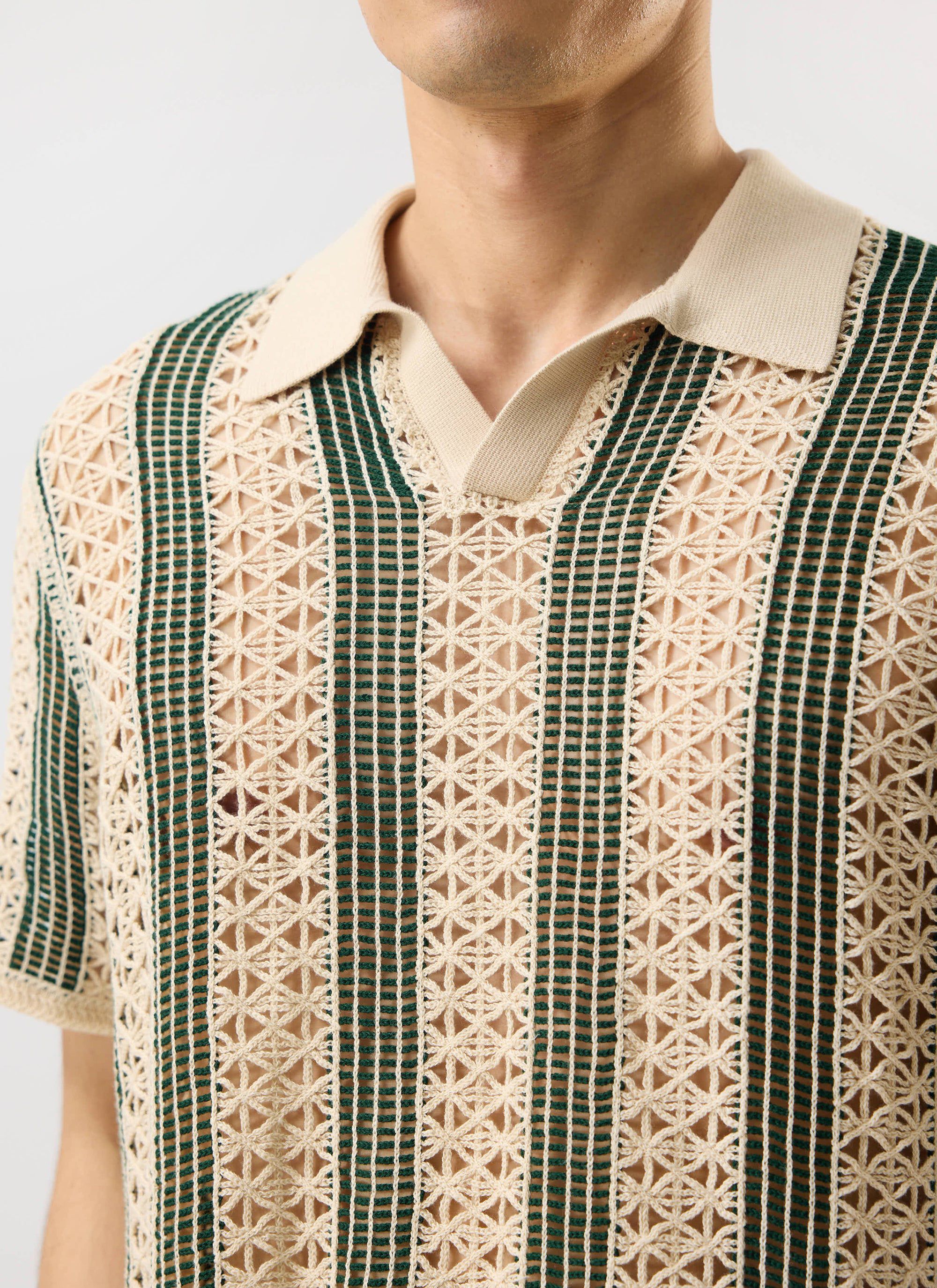 A close-up of the Percival Sarti Knitted Polo Shirt in ecru and forest green, showing the intricate crochet knit detail.