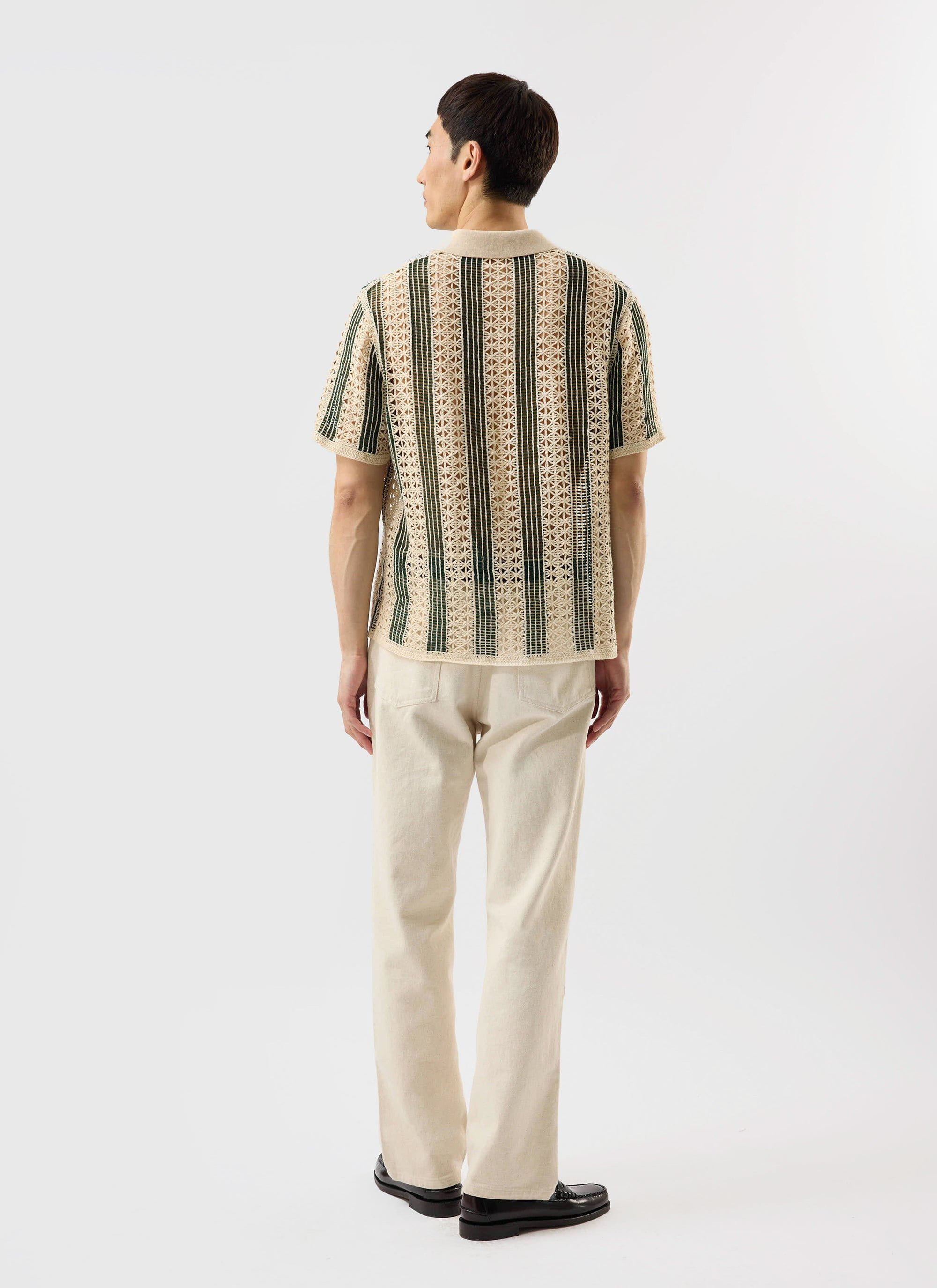 Back view of a model wearing the Percival Sarti crochet polo shirt in ecru with forest green vertical stripes.