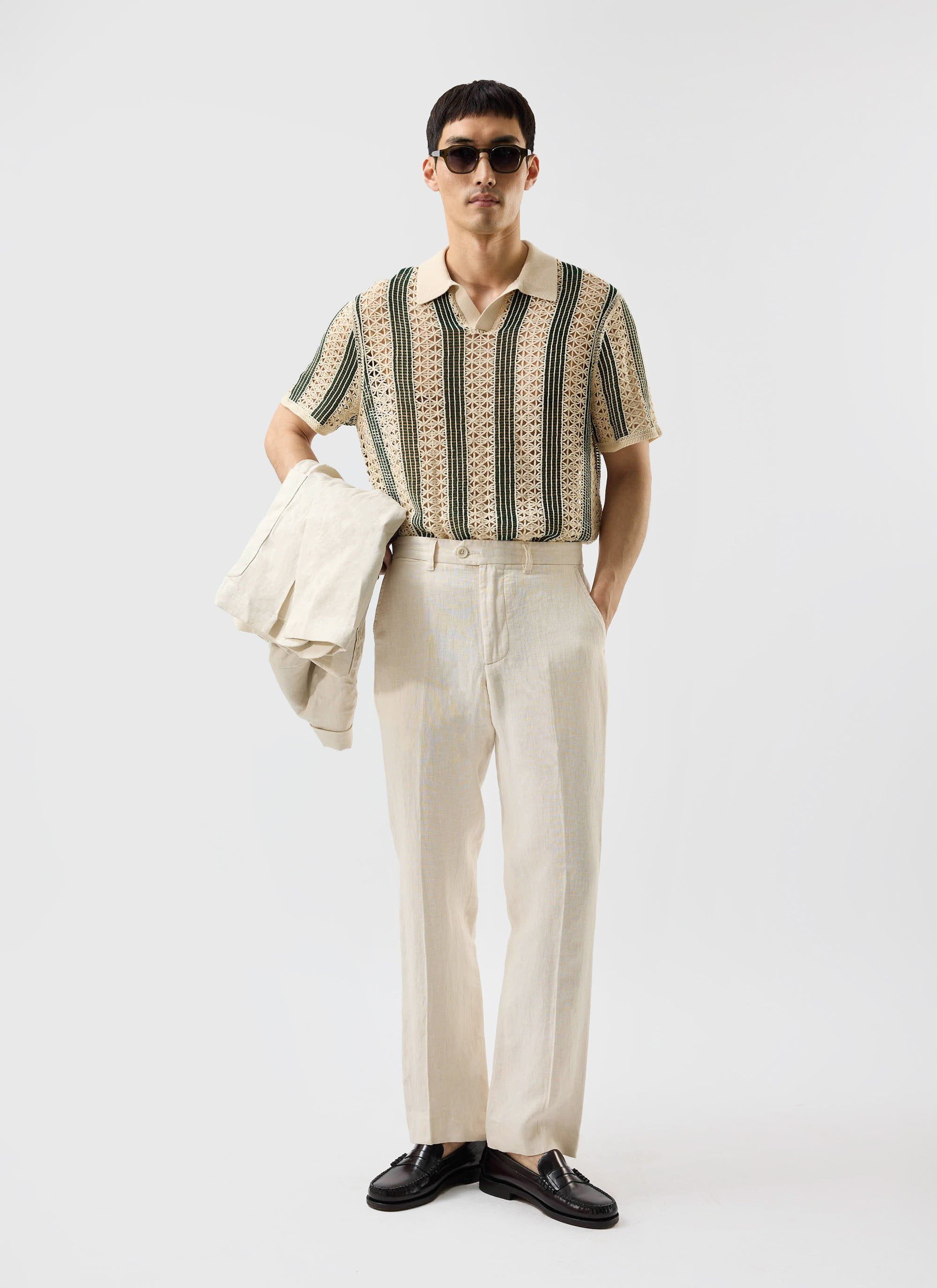 A model wears the Percival Sarti Knitted Polo in ecru and forest green, styled with cream trousers and sunglasses.