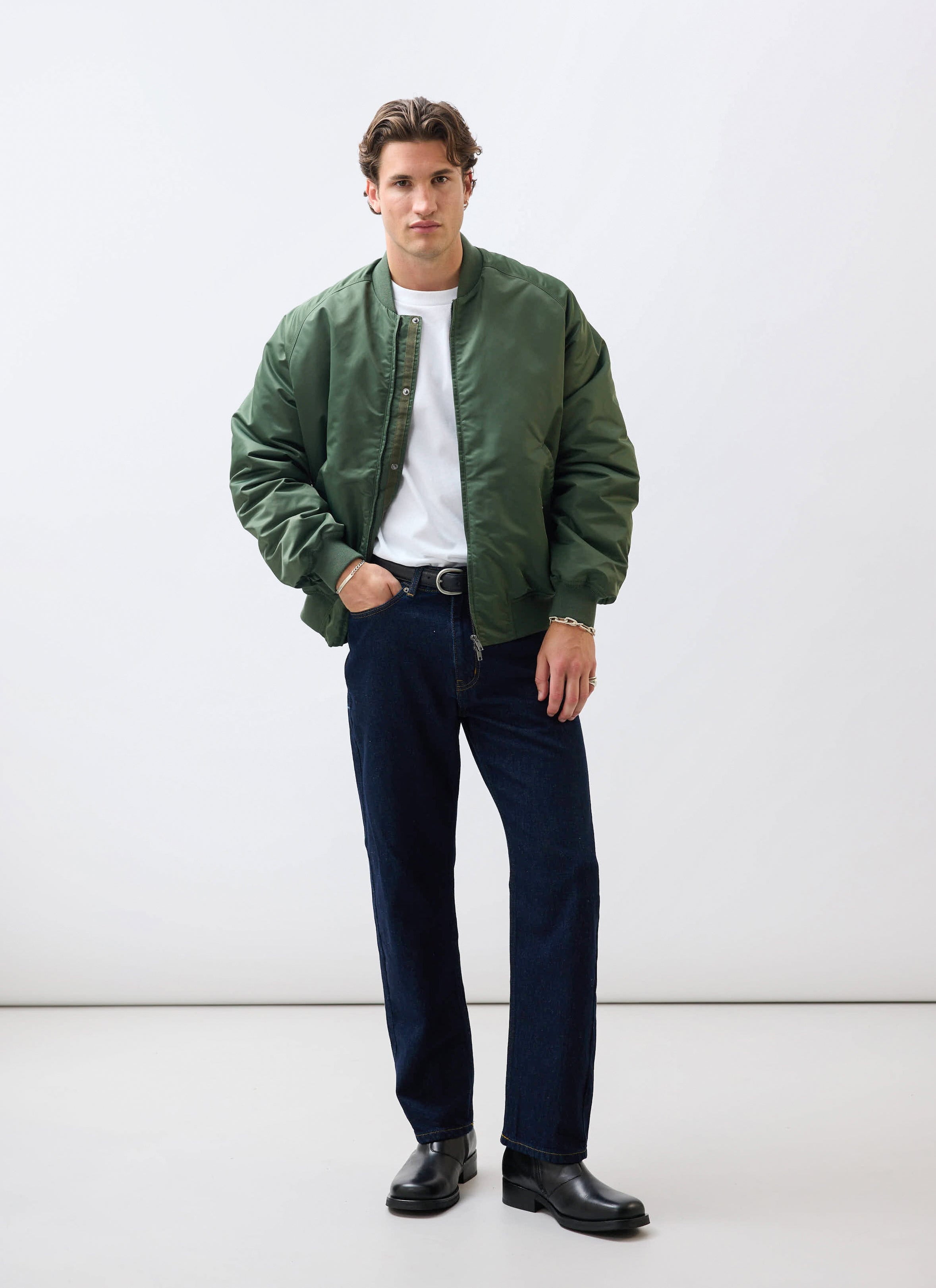 A male model wears the Percival forest green nylon bomber jacket, styled with a white t-shirt and dark jeans.