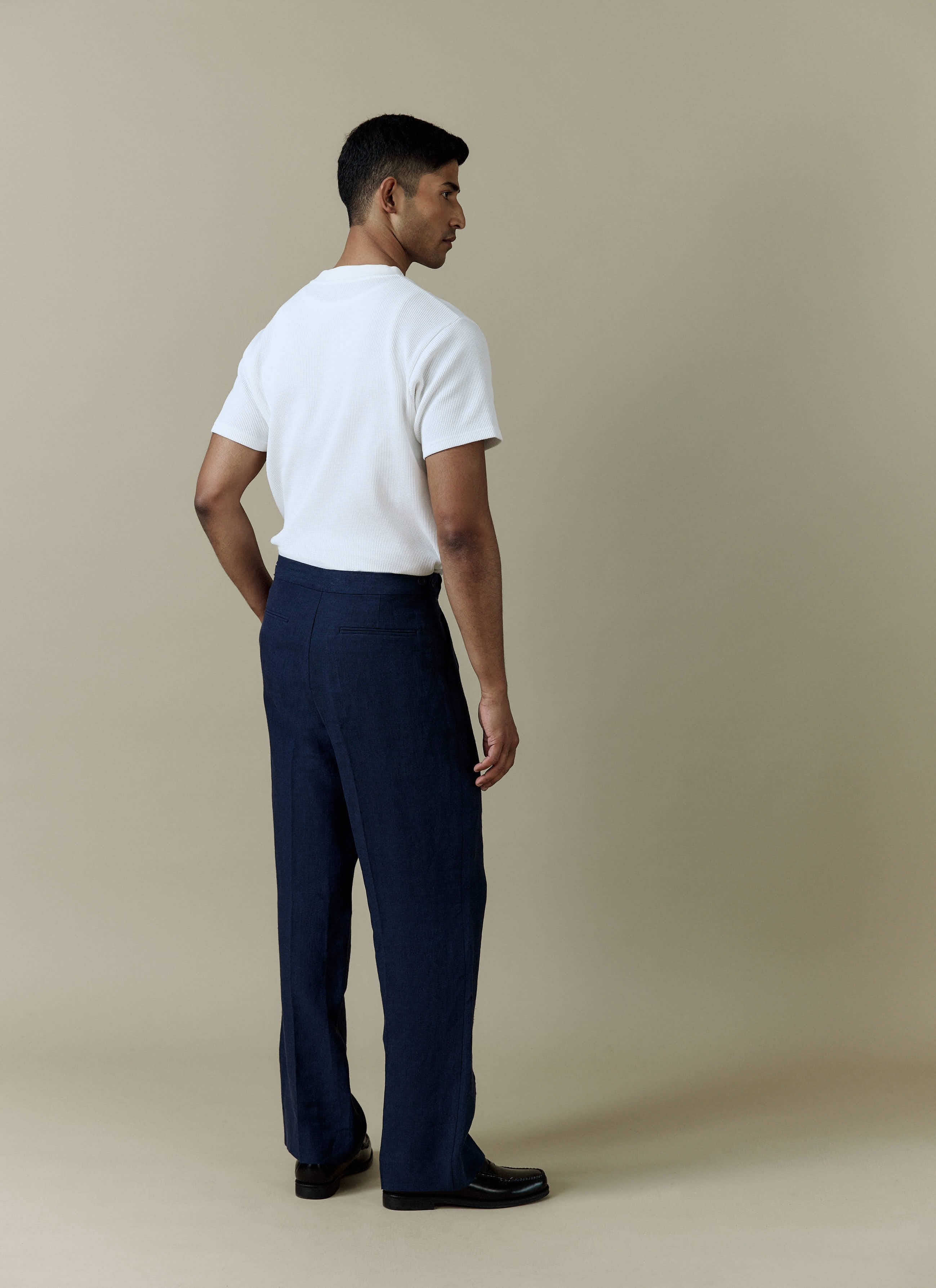 A model seen from behind wearing the Percival navy linen Pleated Tailored Trousers to showcase their relaxed, wide-leg fit.