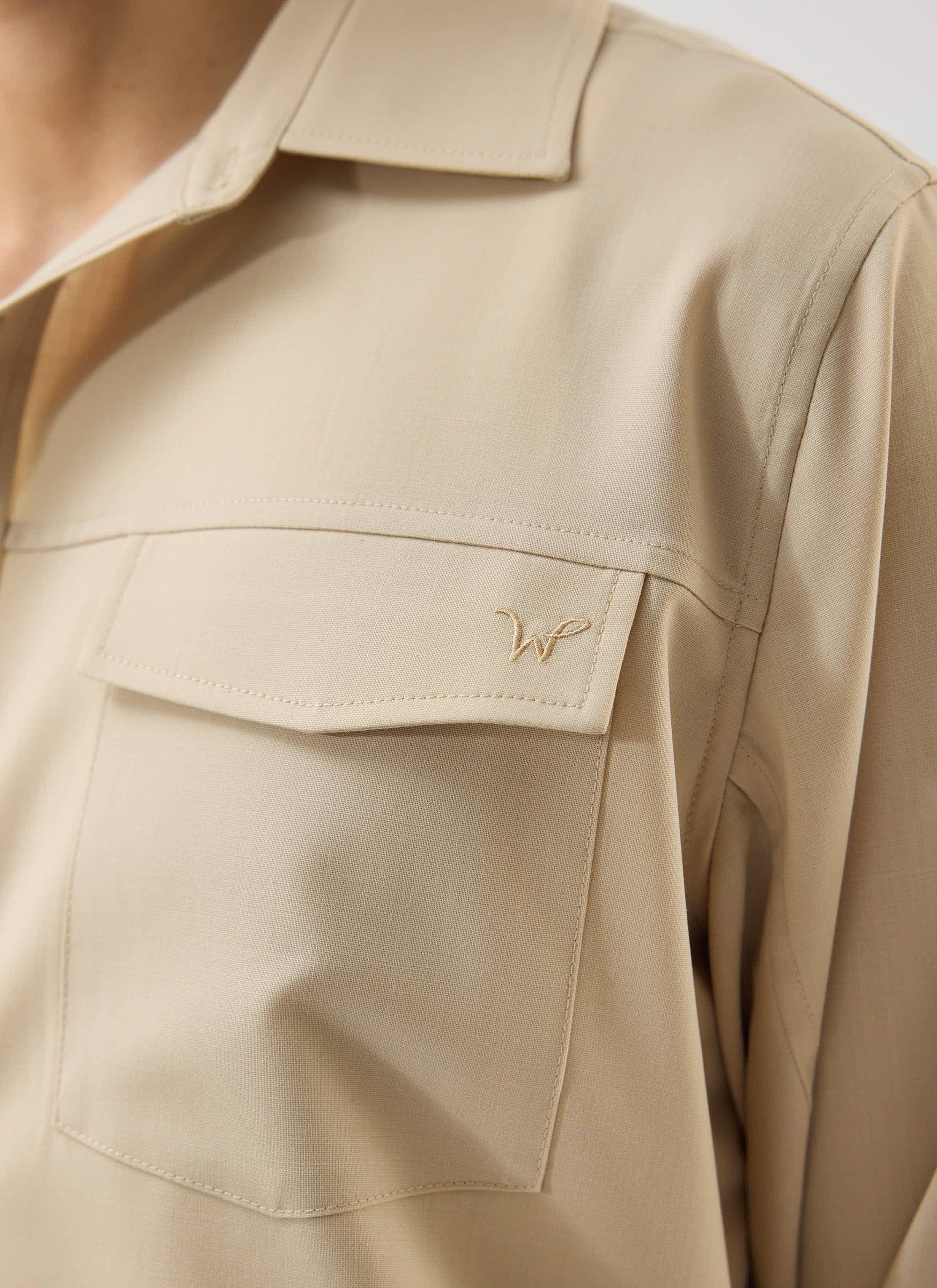 A close-up of the Percival x Warren Safari Shirt in camel beige, showing the tonal 'W' embroidery on the chest pocket.