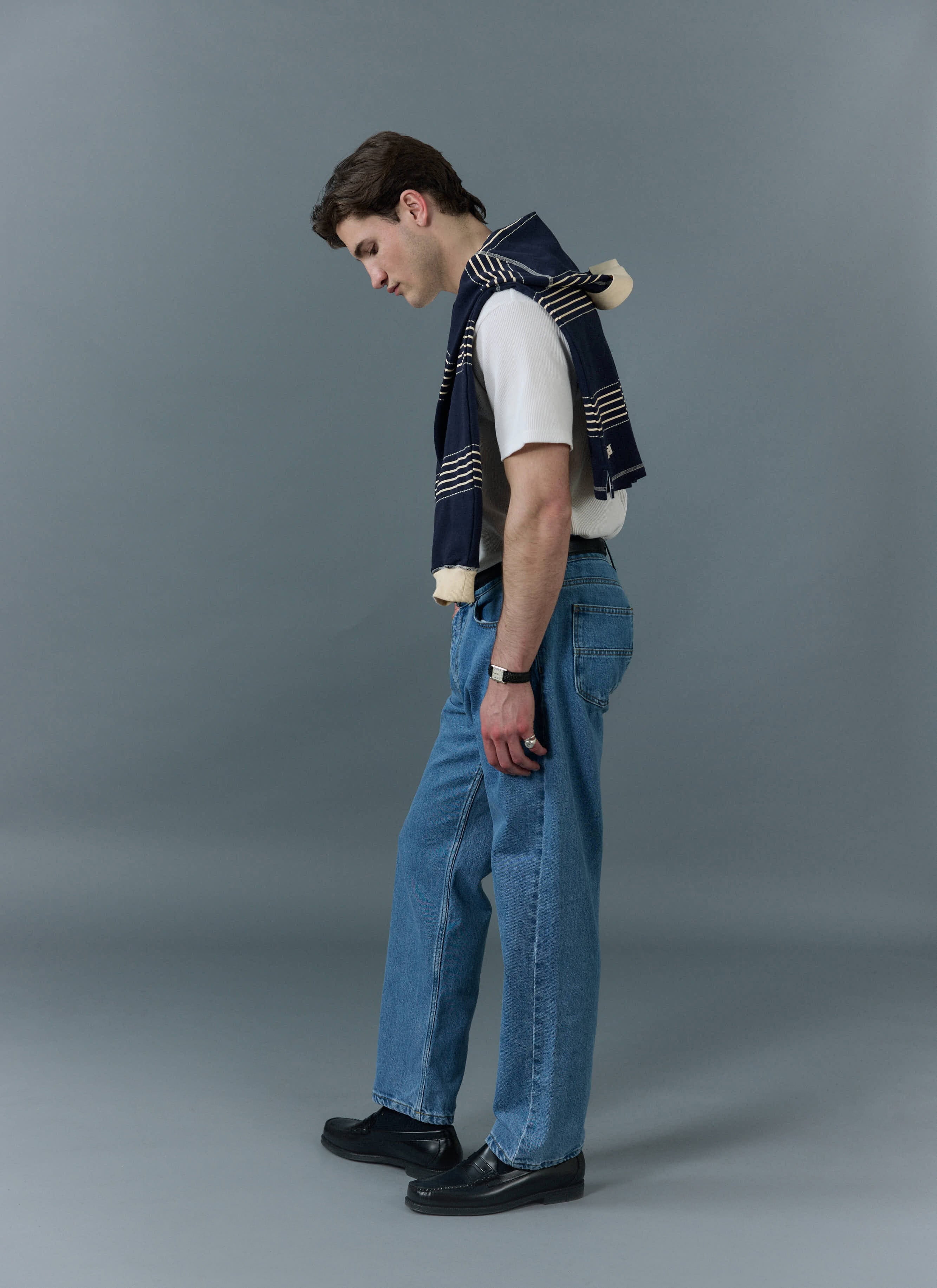 A model wears Percival light wash straight leg jeans with a white t-shirt, black loafers, and a striped jumper.