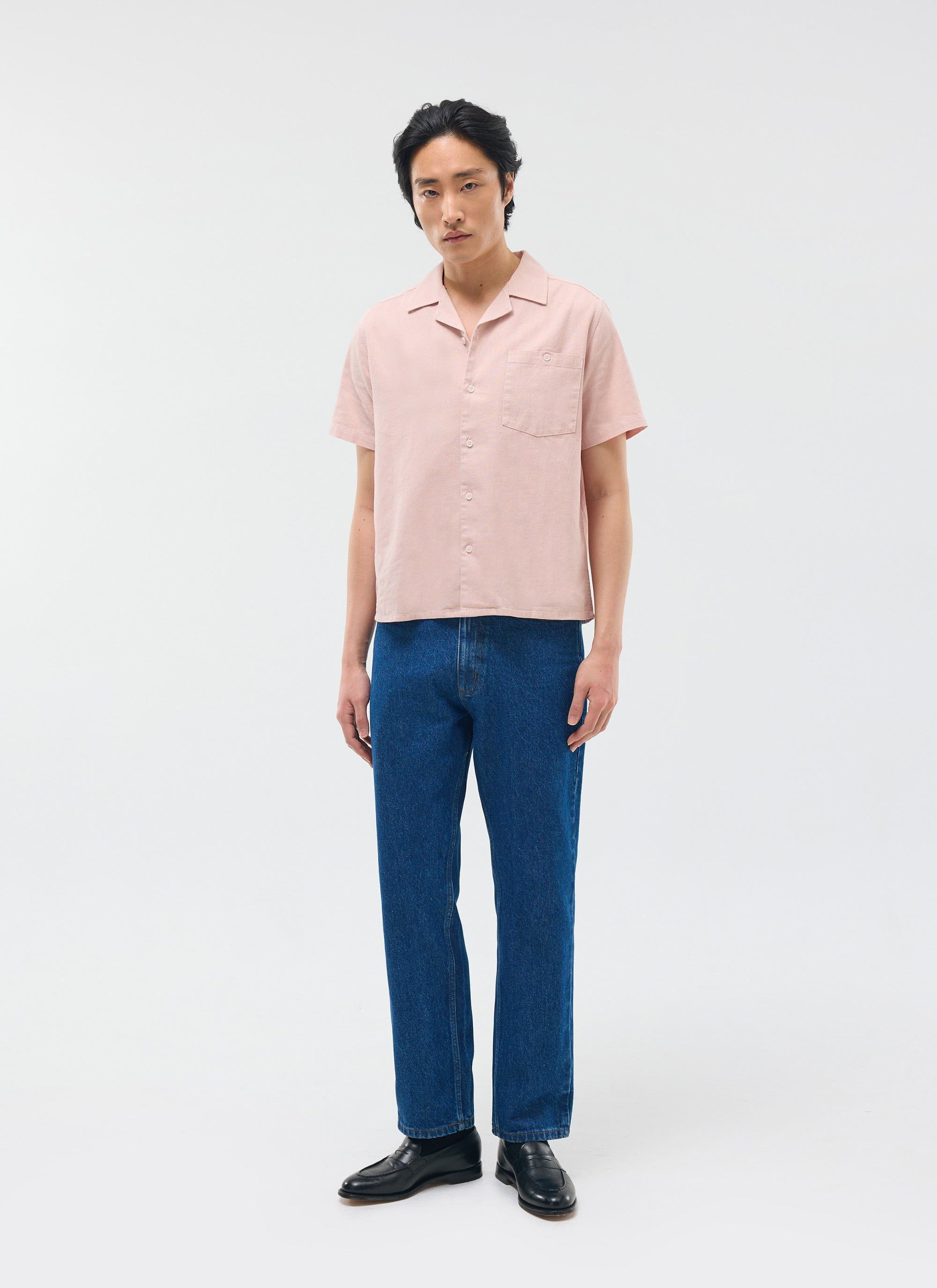 The Percival Short Sleeve Cuban Shirt in dusty pink linen, worn by a model with dark blue jeans against a studio background.