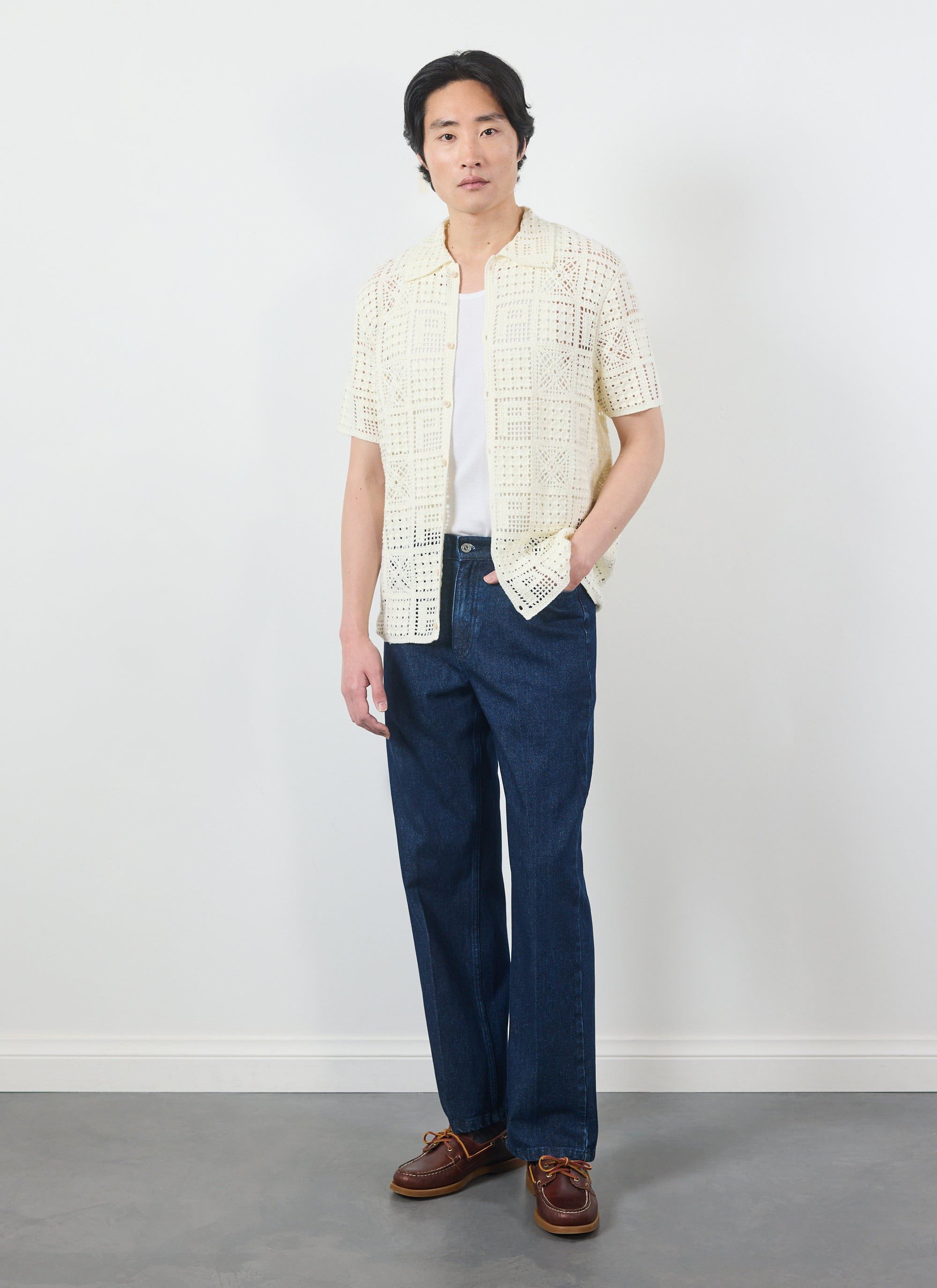 A model wears the Percival Crochet Groundsman Shirt in ecru, styled open over a t-shirt with dark jeans and boat shoes.