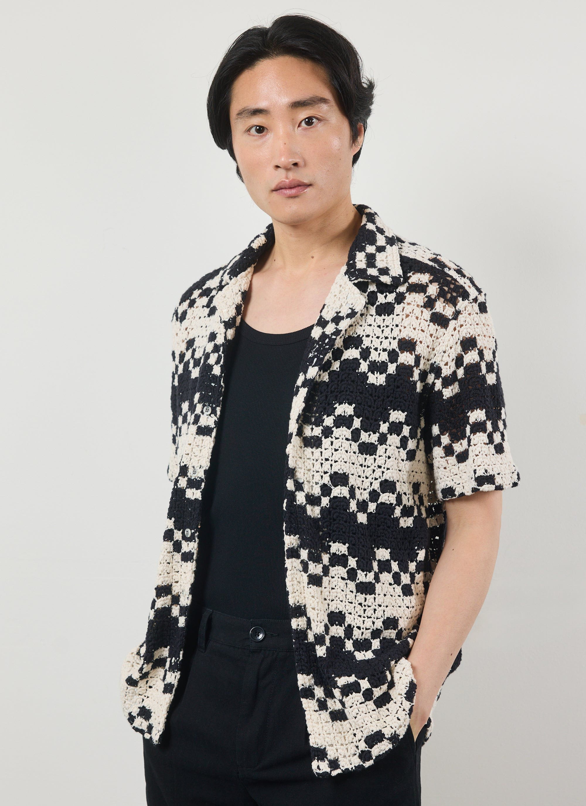A model wears the Percival Naples Crochet Cuban Shirt in ecru and black, styled open over a black vest and trousers.
