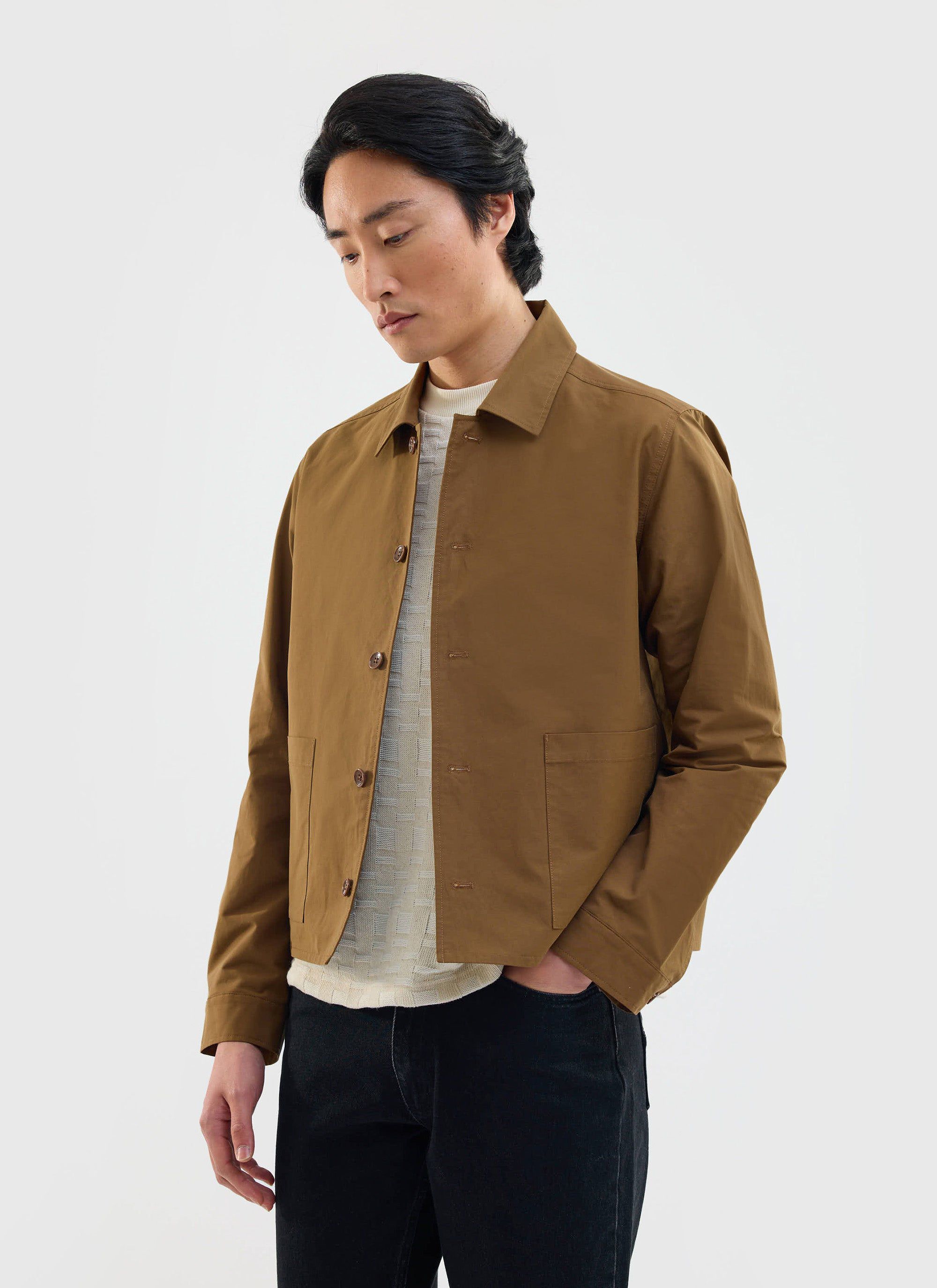 A man models the Percival Boxy Cropped Pocket Overshirt in brown, styled with a jumper and jeans against a white background.