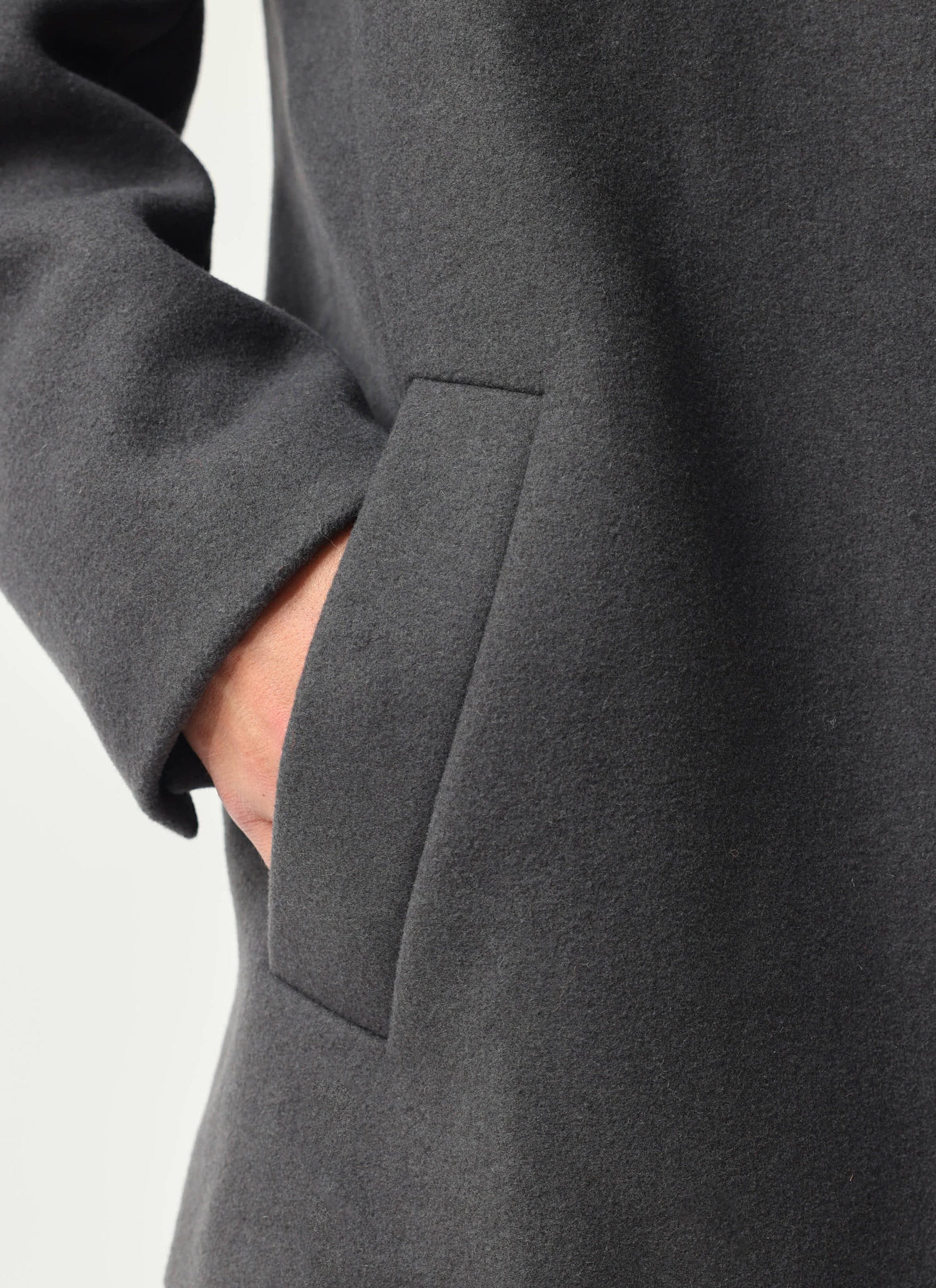 A close-up shot of the welt pocket detail on the charcoal Melton Wool Peacoat from Percival, with a hand tucked inside.