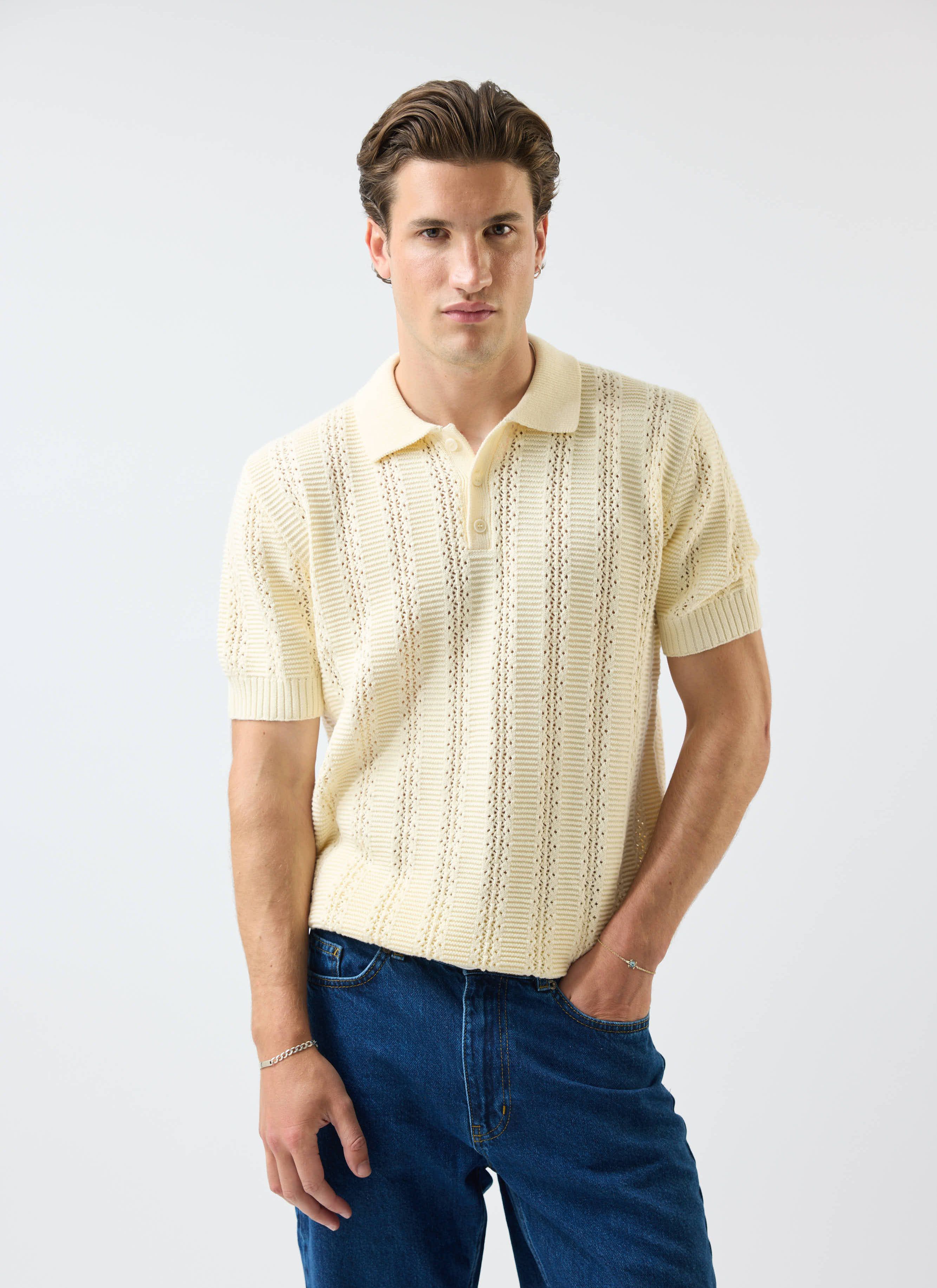A model wears the Percival Addendum Knitted Polo Shirt in ecru cream, showing off its detailed tonal jacquard knit.