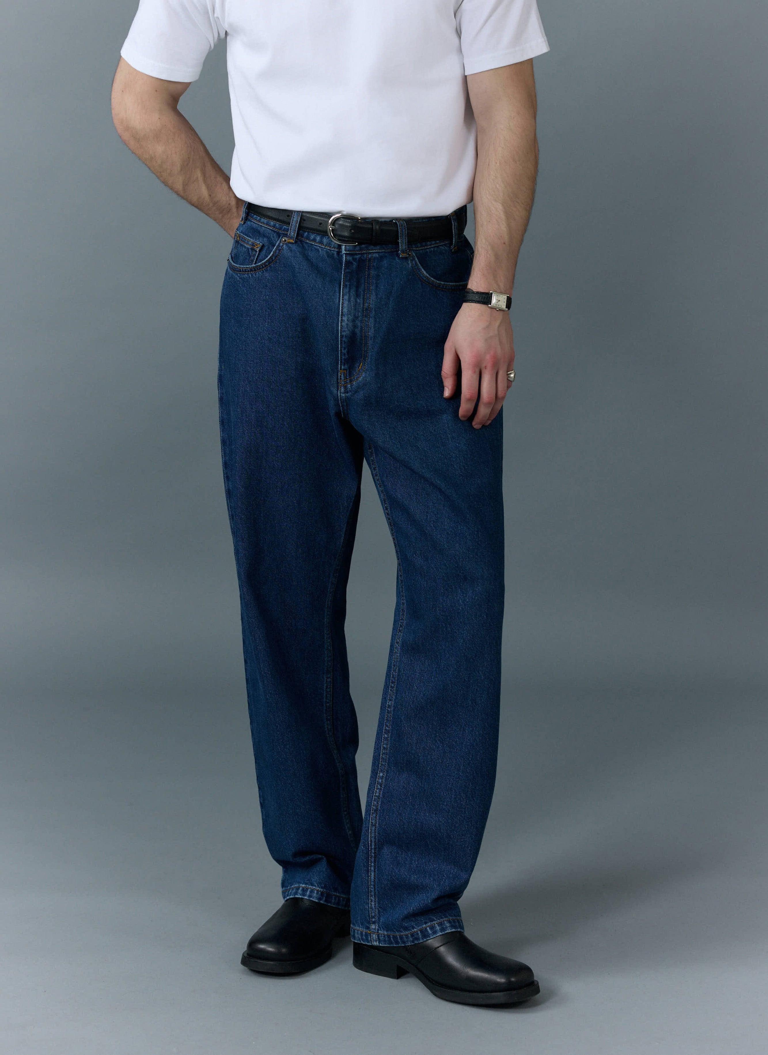 A model wears the Percival Wide Leg Denim Jeans in mid-wash blue, styled with a white t-shirt and black leather shoes.