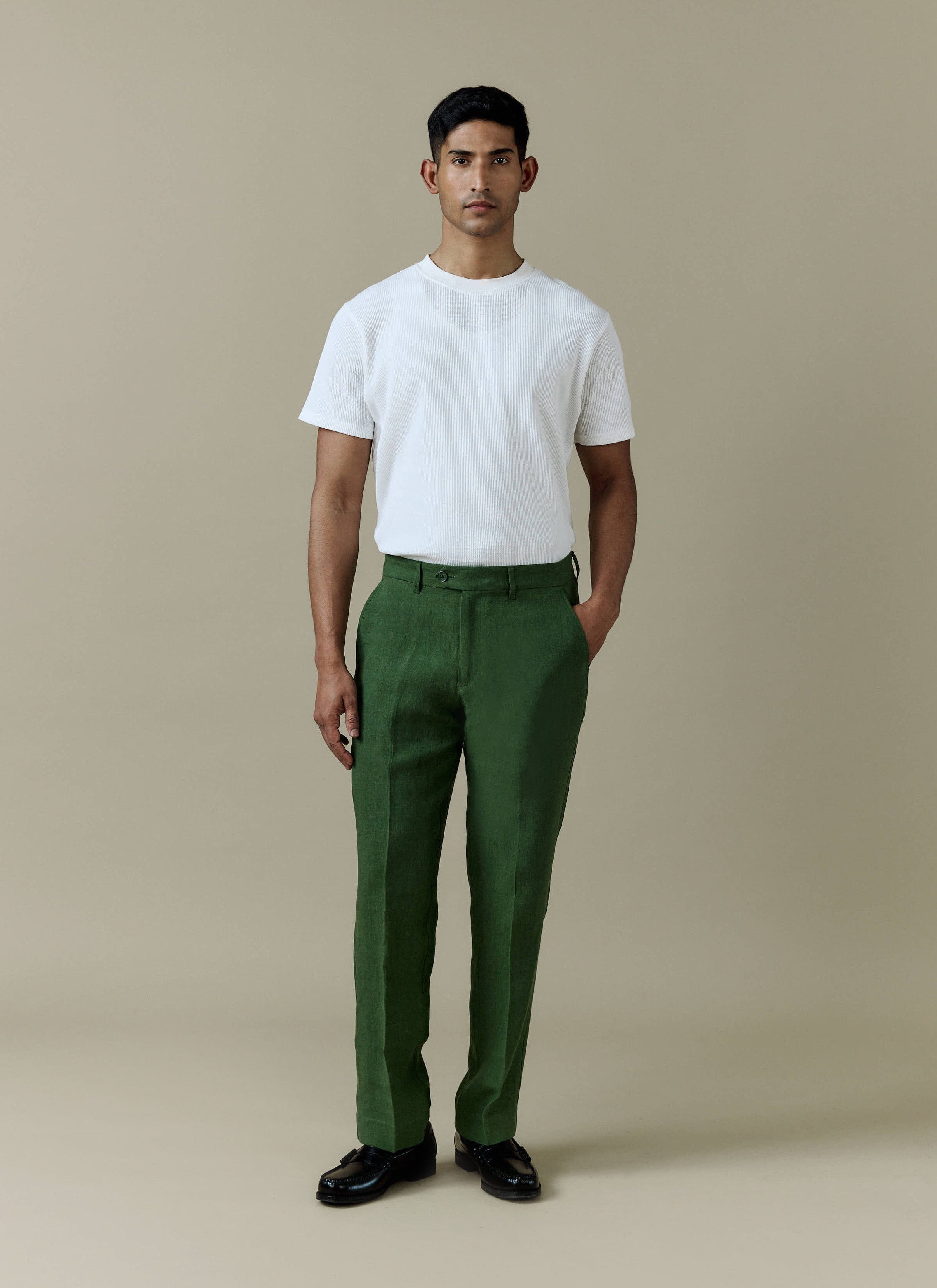 A model wearing the Percival Tailored Linen Trousers in forest green, styled with a white t-shirt.