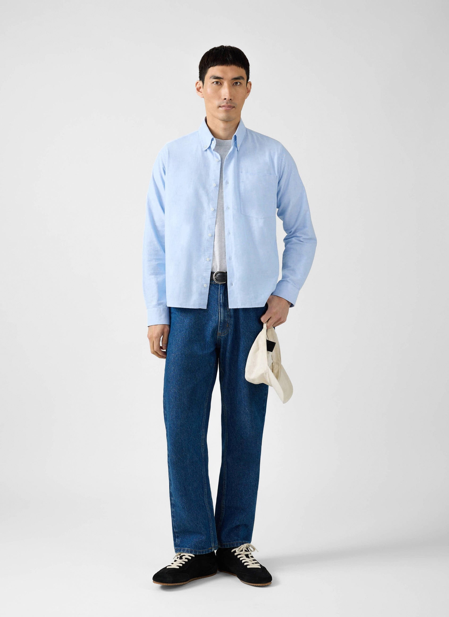 A model wears the Percival Oxford Regular Shirt in light blue, worn open over a t-shirt and styled with dark blue jeans.