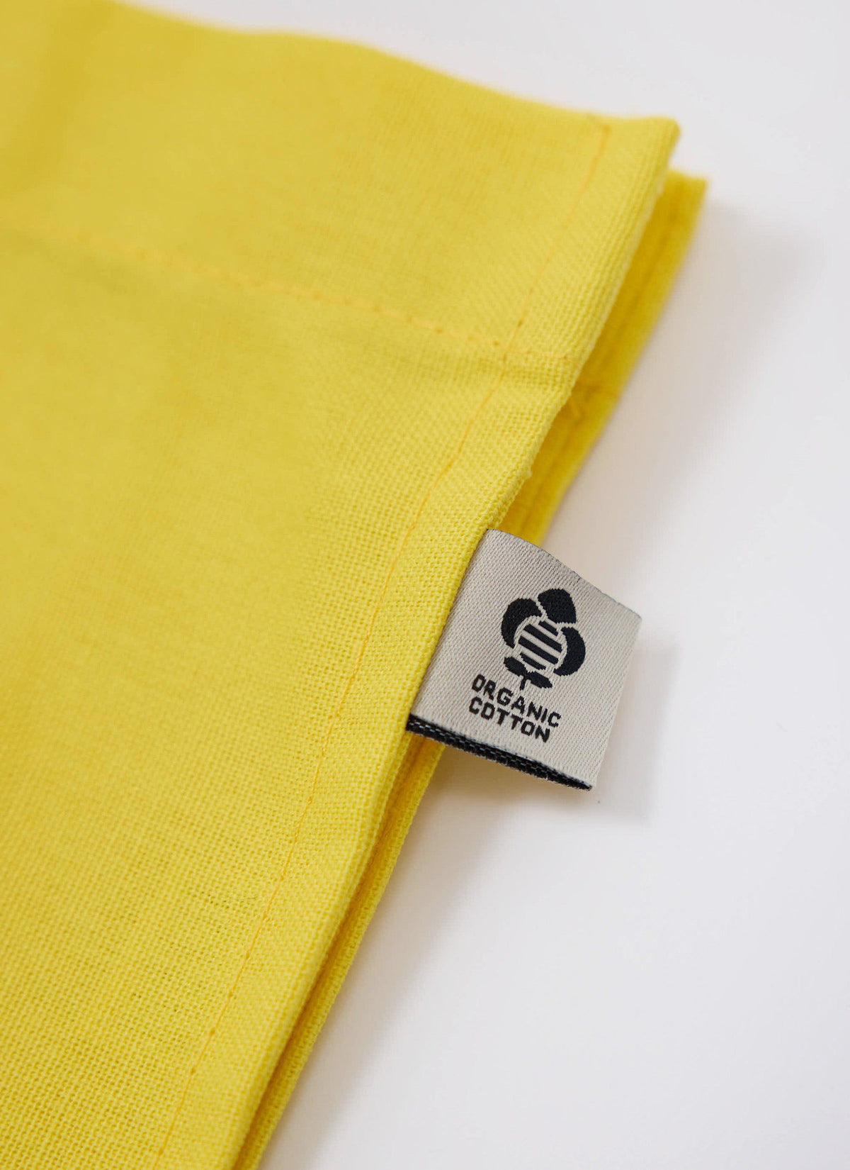 A close-up of the organic cotton label on the yellow tote bag from the Percival x The Gorilla Brand collaboration.