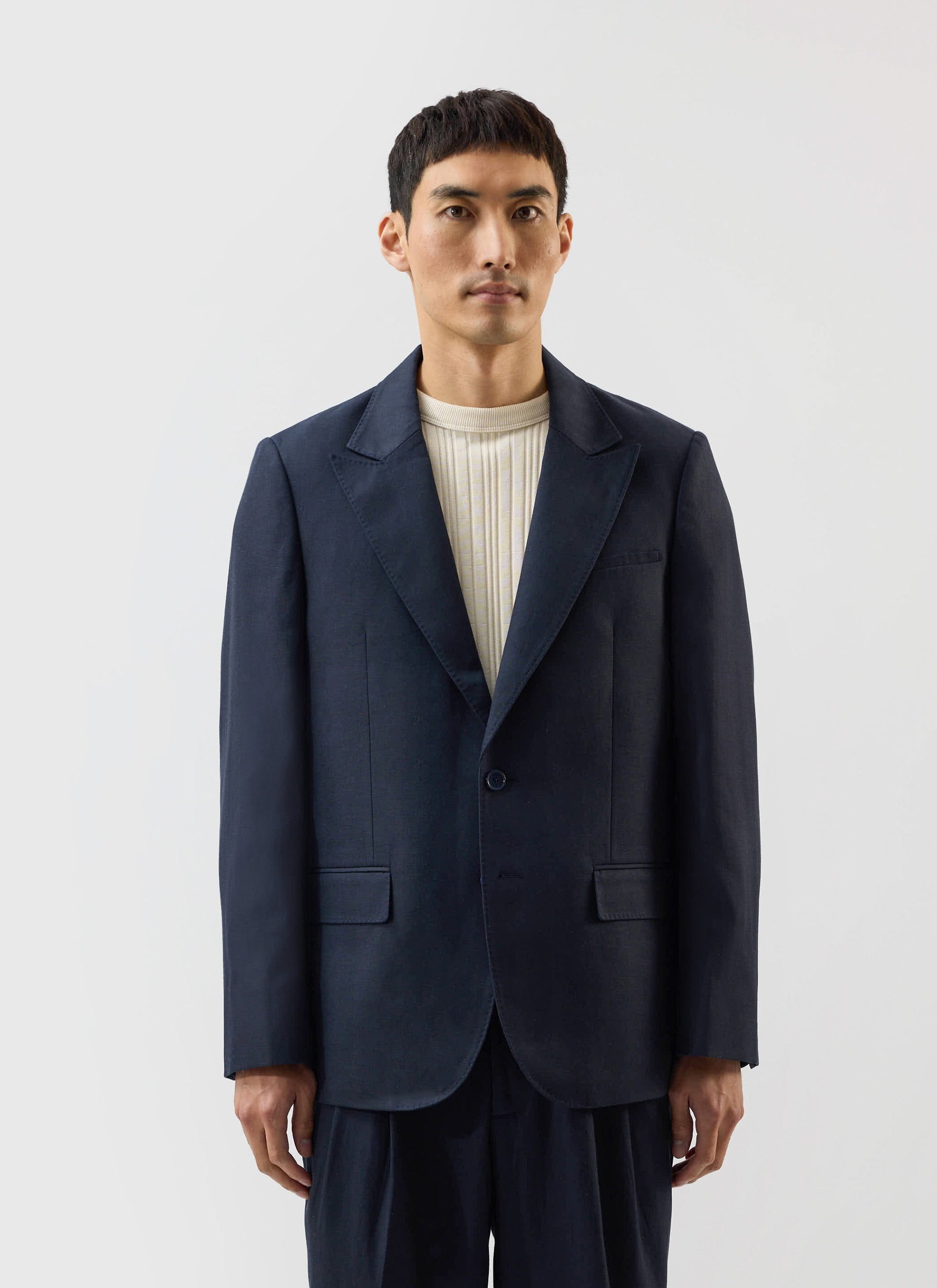 A man models the Percival x Warren Lyocell Tailored Blazer in navy, styled over a cream ribbed knit top.