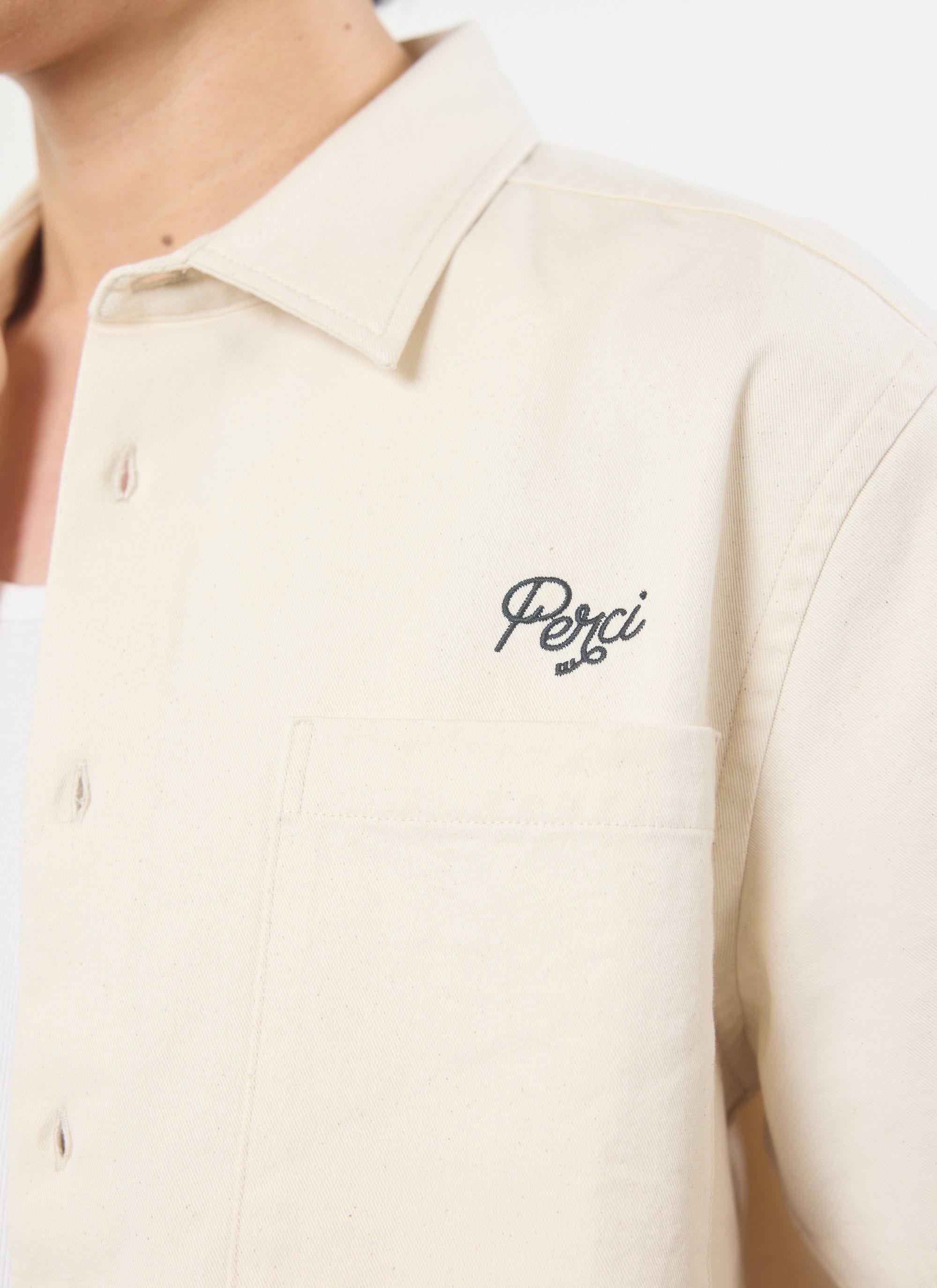 A close-up of the Percival Olive Embroidered Cropped Shirt in off-white, showing the 'Perci' logo embroidery on the chest.