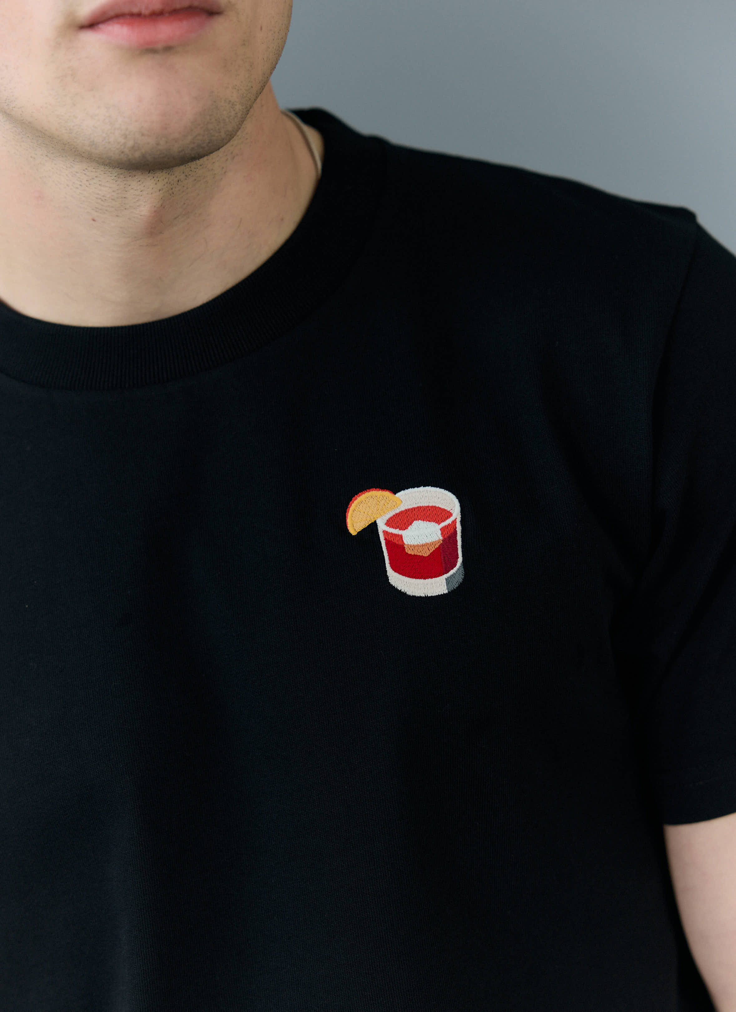 A close-up of the Negroni cocktail embroidery on the chest of the black organic cotton t-shirt from Percival.