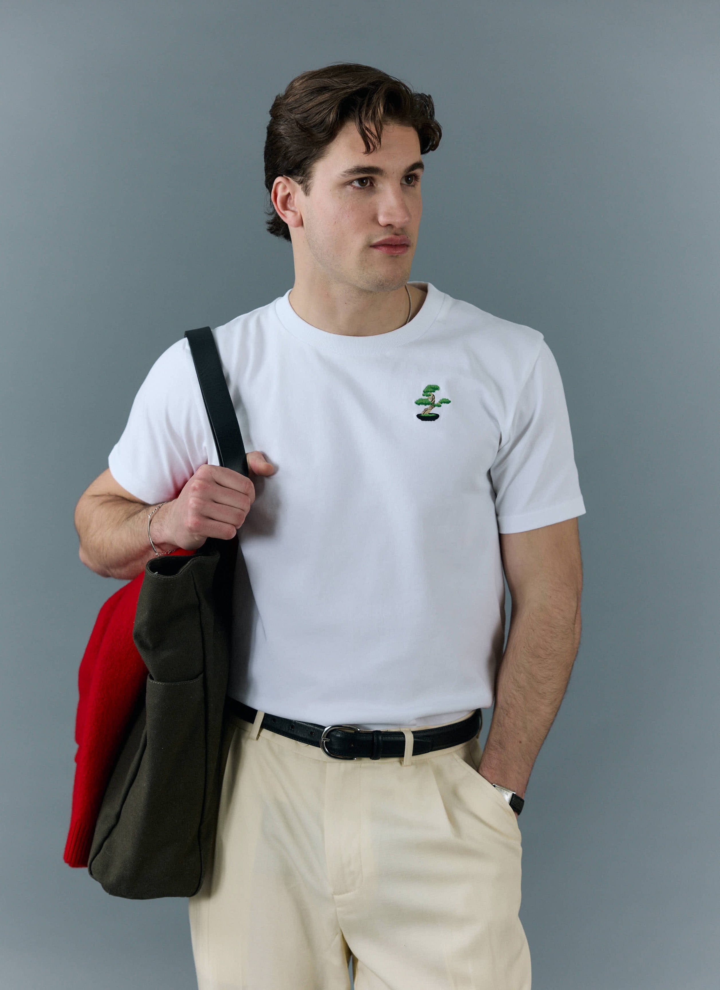 A model wears the white Percival Bonsai tee, with its detailed chest embroidery, styled with cream trousers and a tote bag.